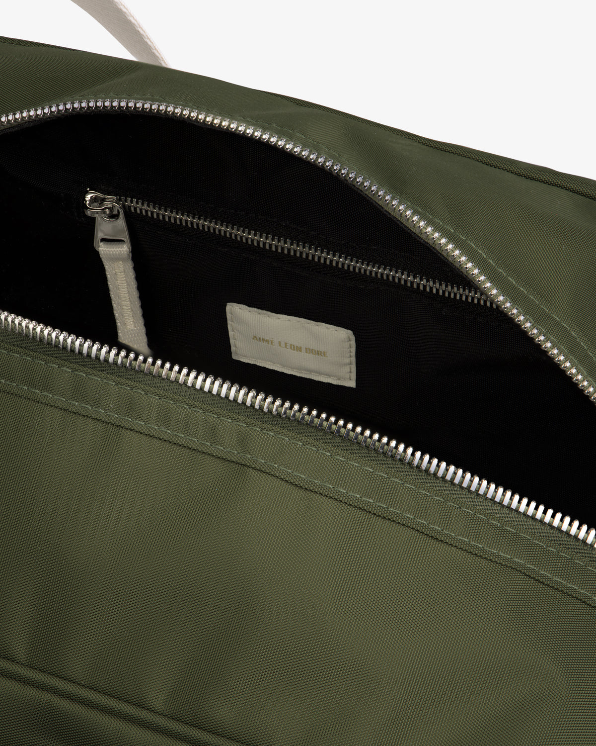 Close-up of an open Nylon Duffle Bag in olive green with a silver zipper, showing interior zip pocket and label.