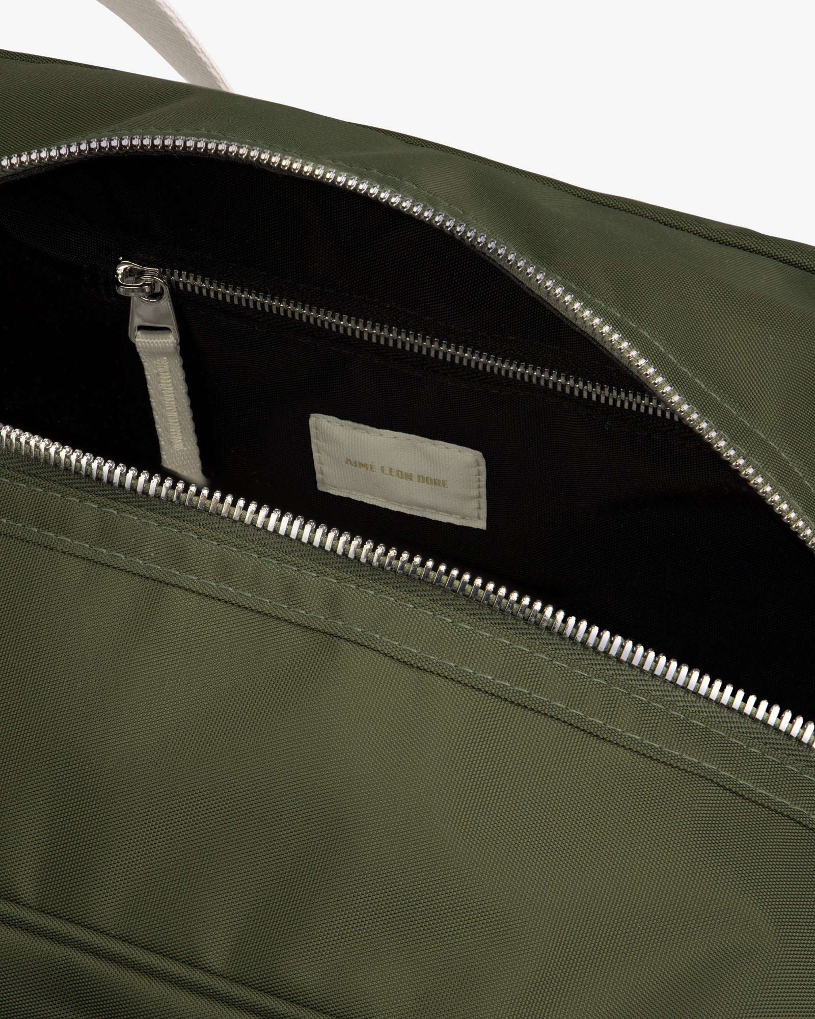 Close-up of an open Nylon Duffle Bag in olive green with a silver zipper, showing interior zip pocket and label.