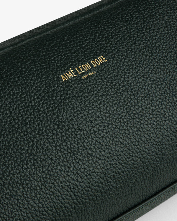 Close-up of a textured dark green Leather Traveler Kit with gold Aimé Leon Dore New York branding embossed.