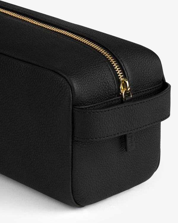 The Leather Traveler Kit—a black leather toiletry bag with a gold zipper and side handle—on a white background.