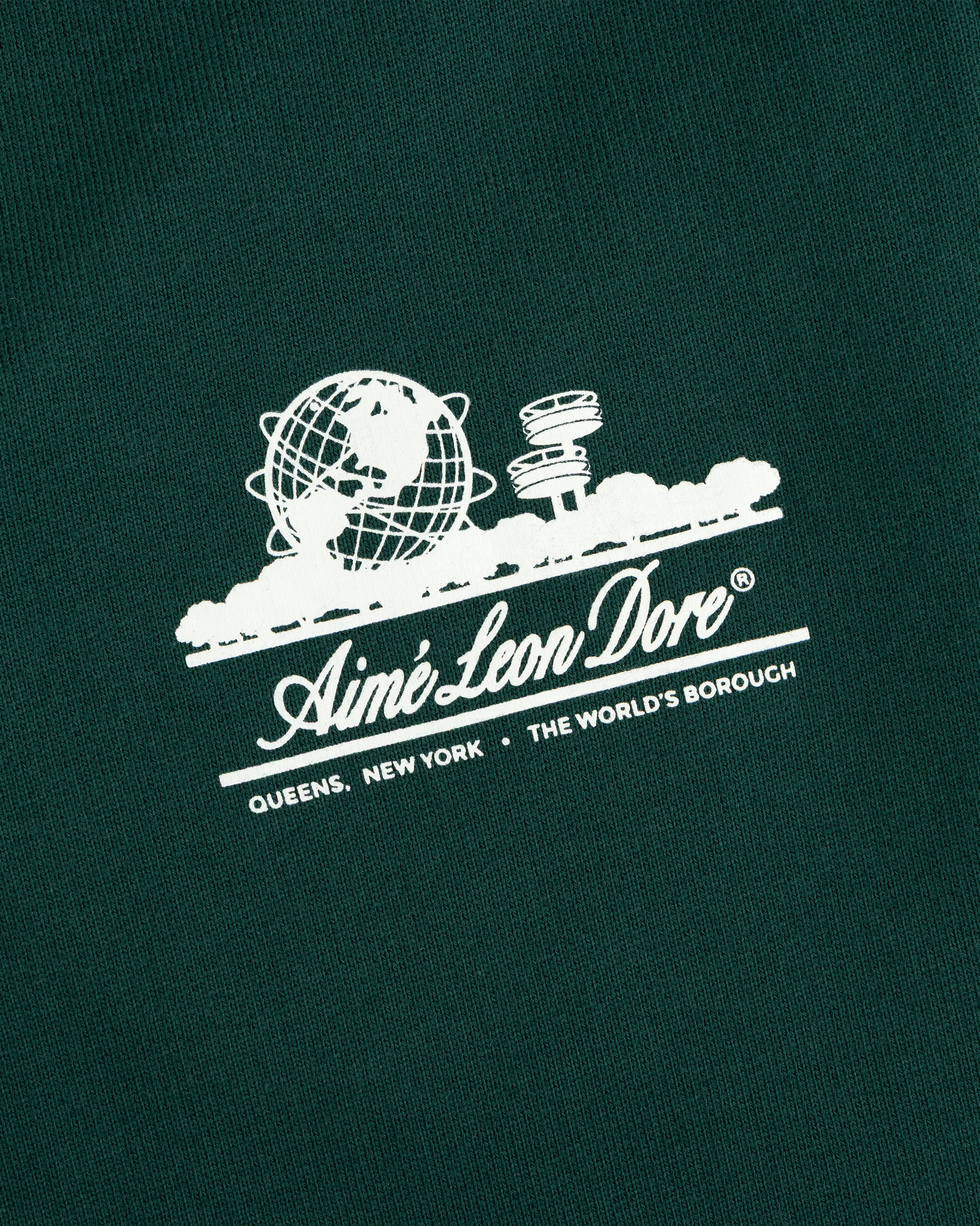 White Aimé Leon Dore Unisphere logo with globe, UFO, and text on dark green Unisphere Sweatpants.