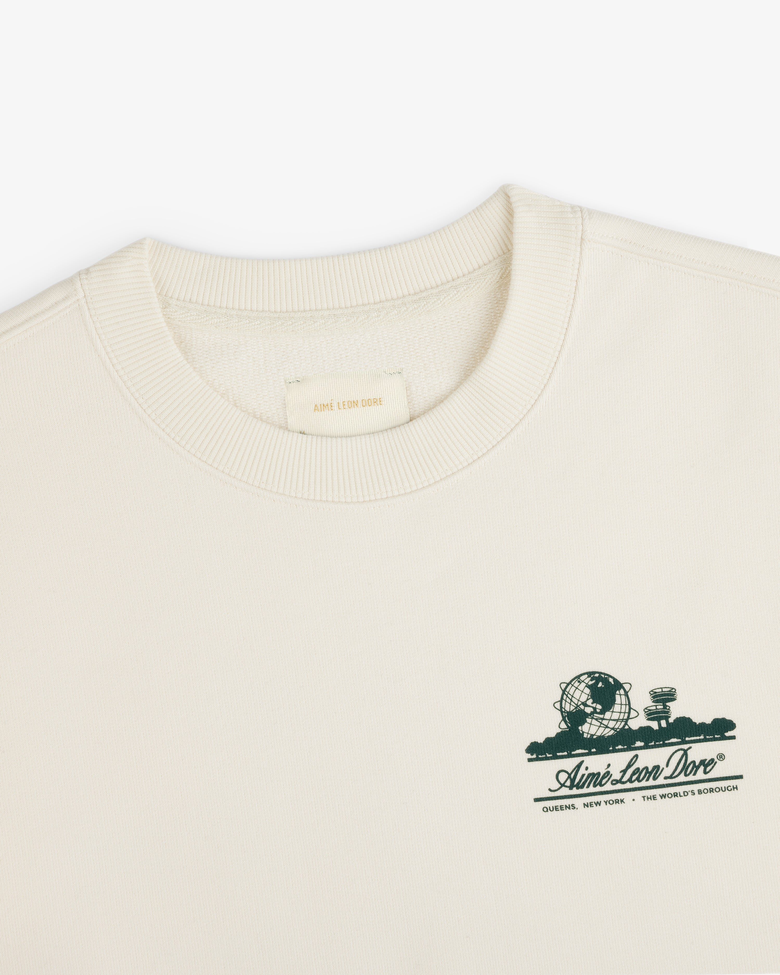 Cream Unisphere Crewneck Sweatshirt with small green graphic and Aimé Leon Dore text on the left chest.