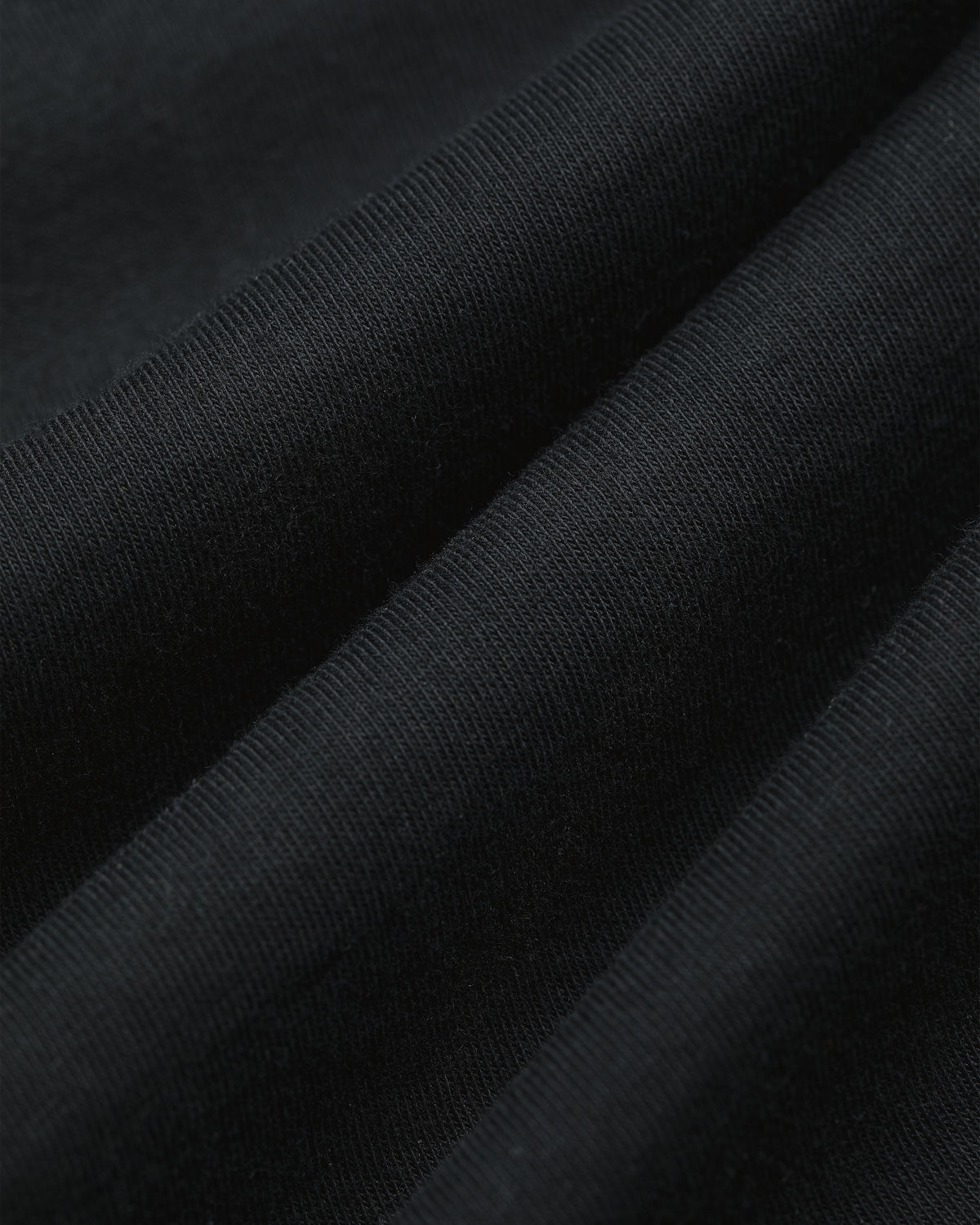 Close-up of black T-Shirt 3-Pack ribbed fabric with visible texture and gentle diagonal folds.