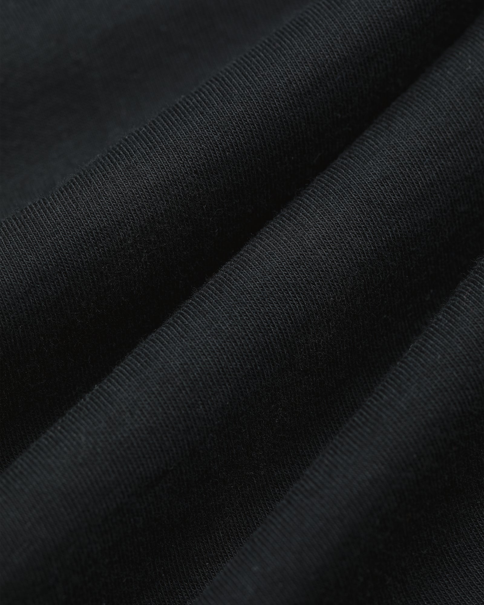Close-up of black T-Shirt 3-Pack ribbed fabric with visible texture and gentle diagonal folds.