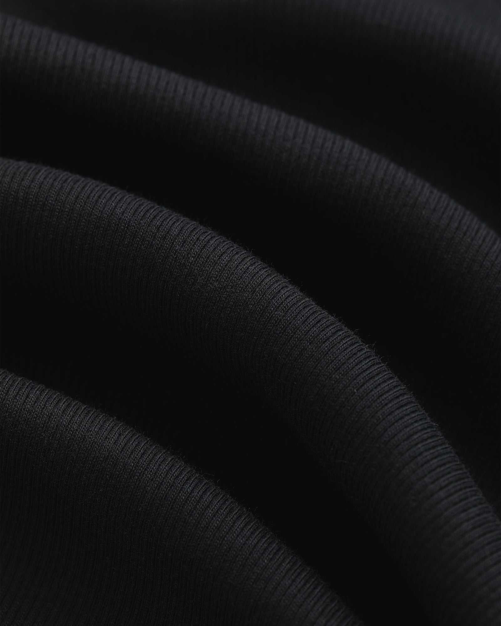 Close-up of black ribbed Tank Top 3-Pack fabric with soft folds and visible textured lines.