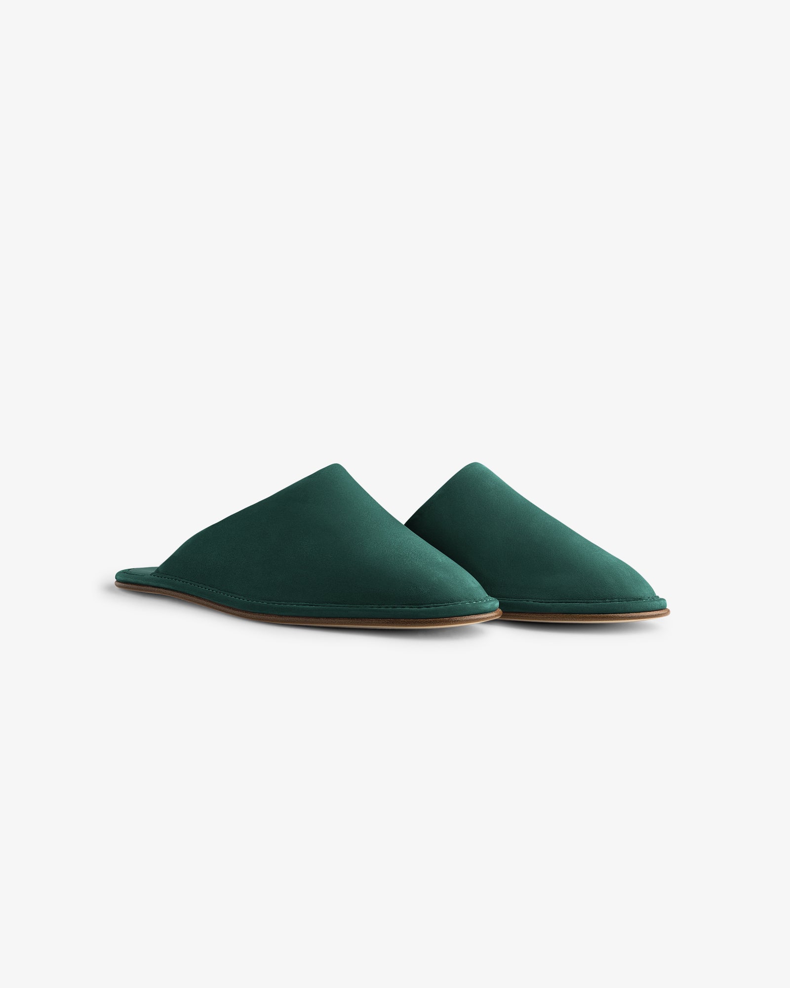 The Nubuck Travel Slipper is a pair of dark green slip-on slippers with flat brown soles on a white background.