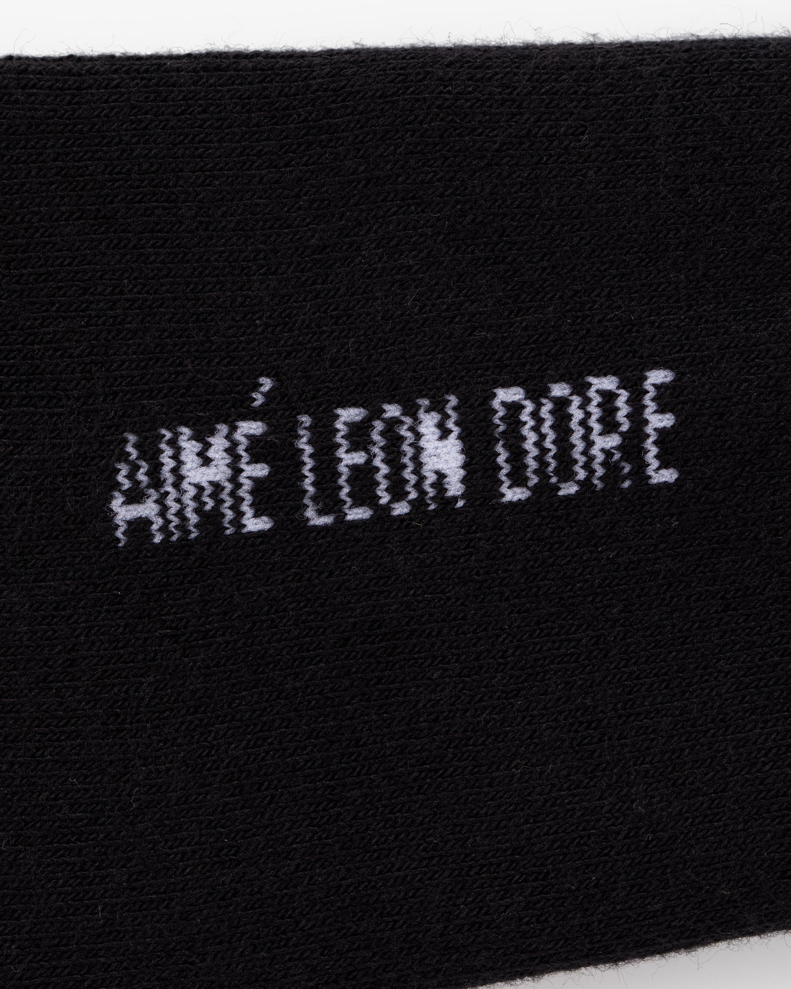 Black fabric crew socks with white embroidered “AIMÉ LEON DORE” text in a distorted, pixelated font. Pack of 3.