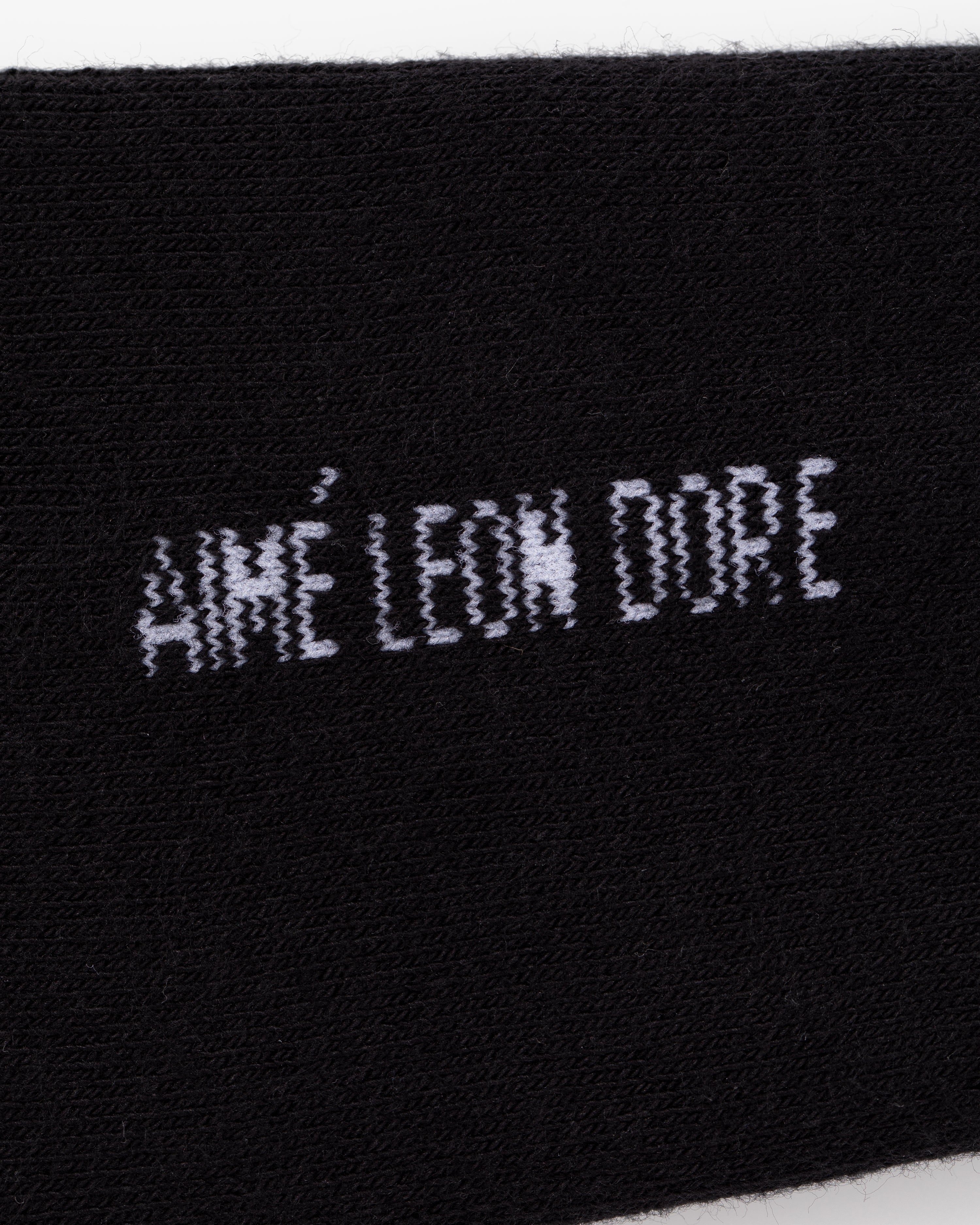Black fabric crew socks with white embroidered “AIMÉ LEON DORE” text in a distorted, pixelated font. Pack of 3.