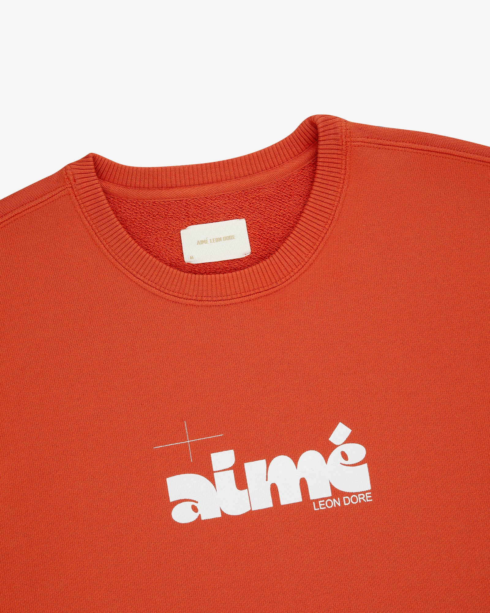 Close-up of an orange Drafting Logo Crewneck Sweatshirt featuring a bold white Aimé Leon Dore logo on the chest.