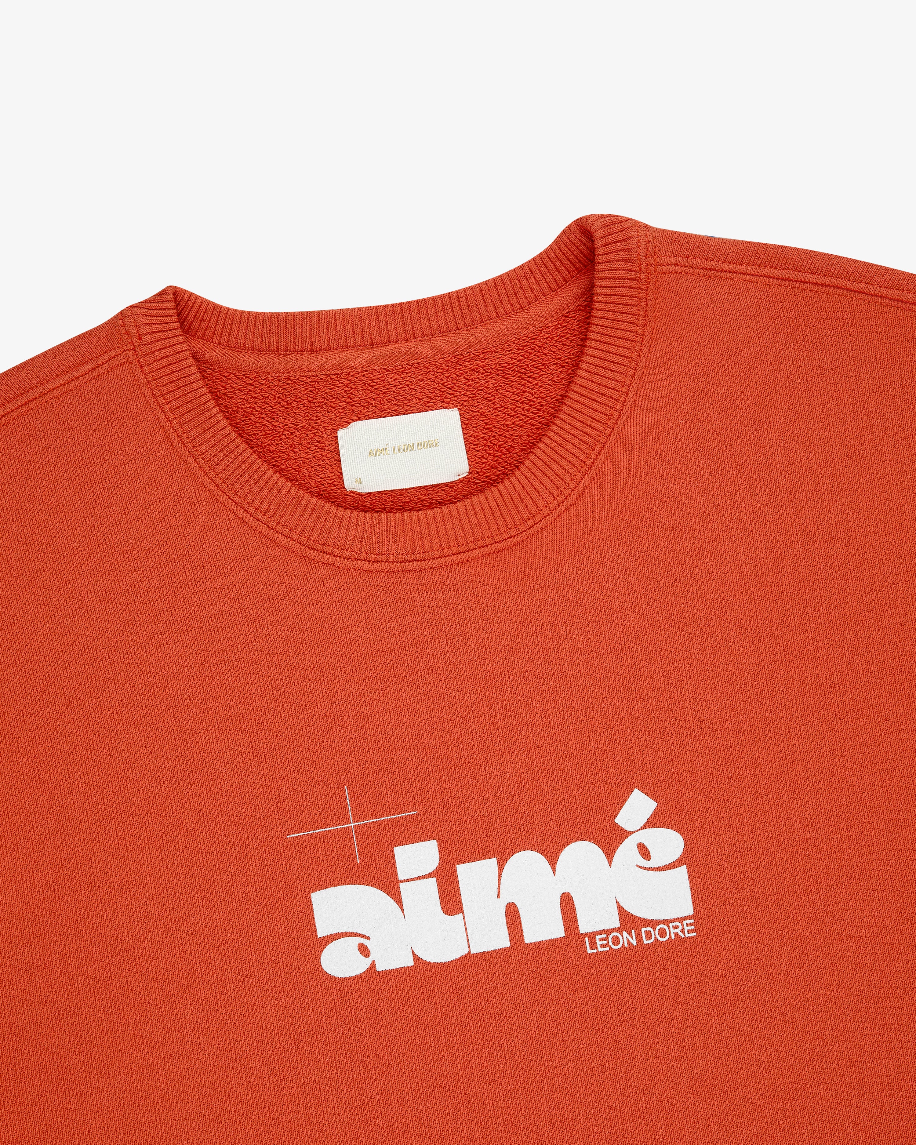 Close-up of an orange Drafting Logo Crewneck Sweatshirt featuring a bold white Aimé Leon Dore logo on the chest.