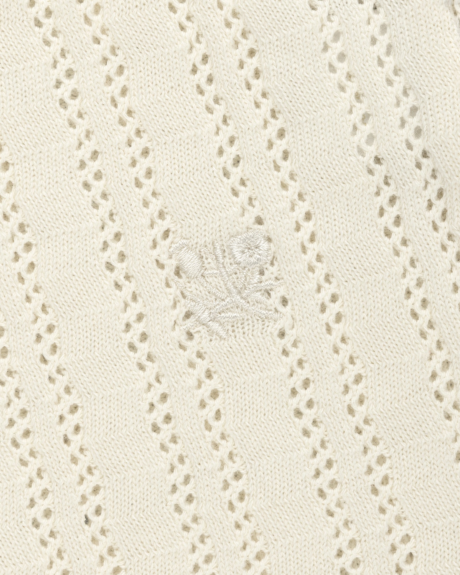 Cream eyelet-knit tank top with diagonal patterns and subtle embroidered floral detail at the center.