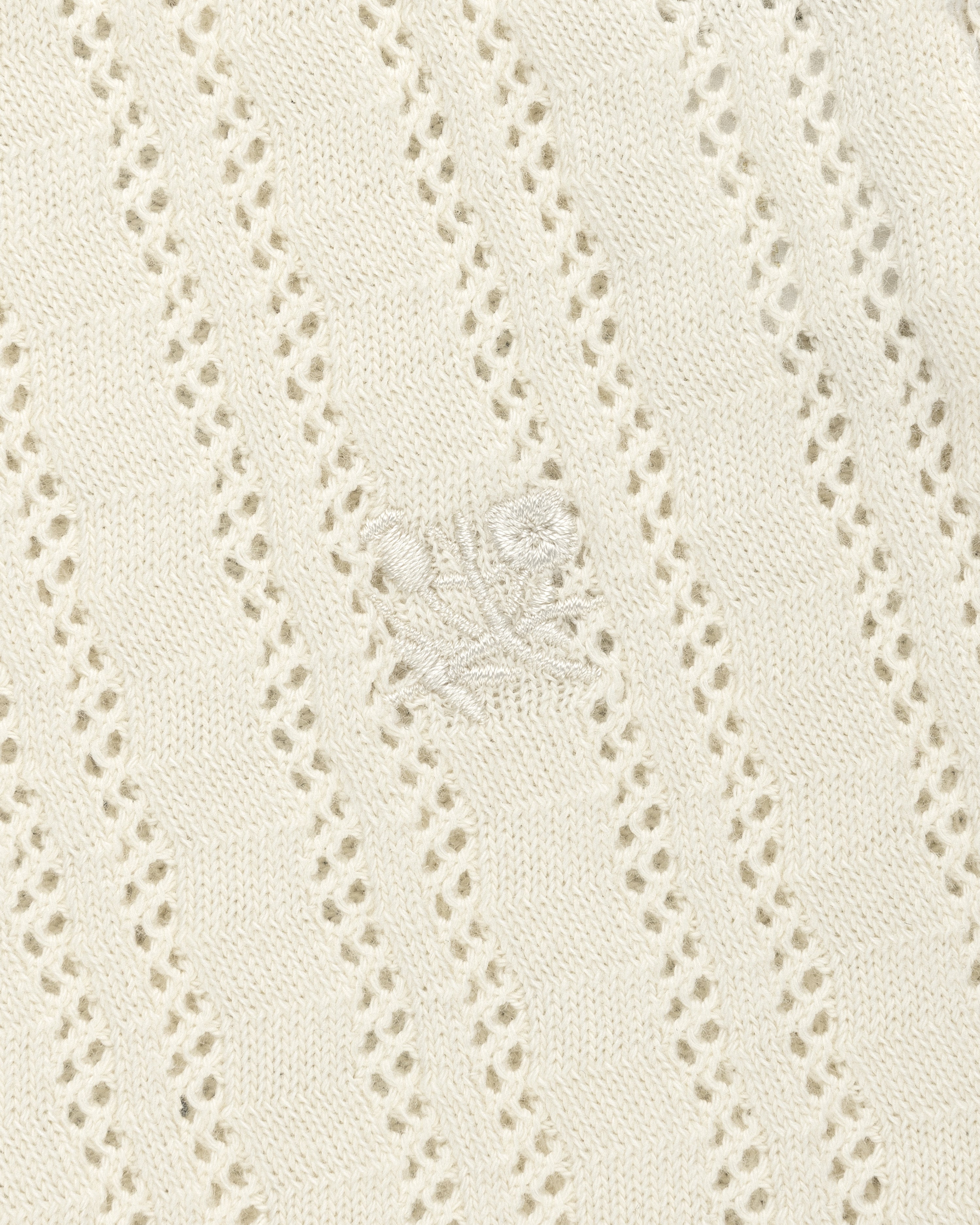 Cream eyelet-knit tank top with diagonal patterns and subtle embroidered floral detail at the center.