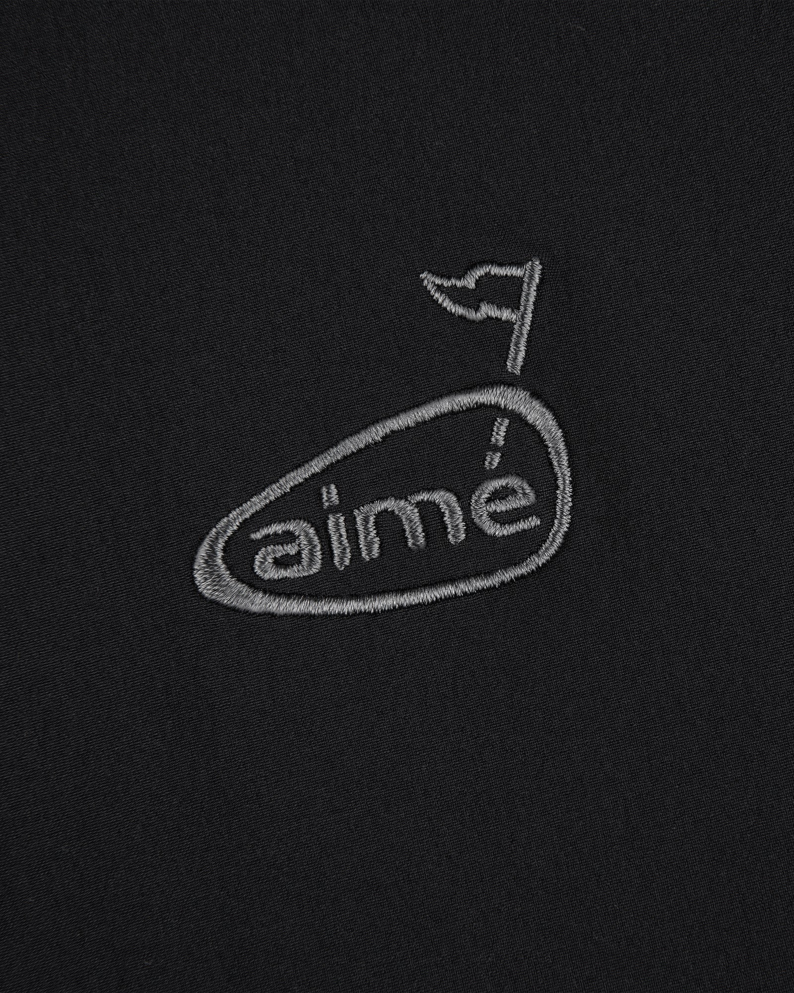 ALD Golf Cordura Tips Jacket: grey aimé logo with flag above the e, embroidered on plain black fabric.