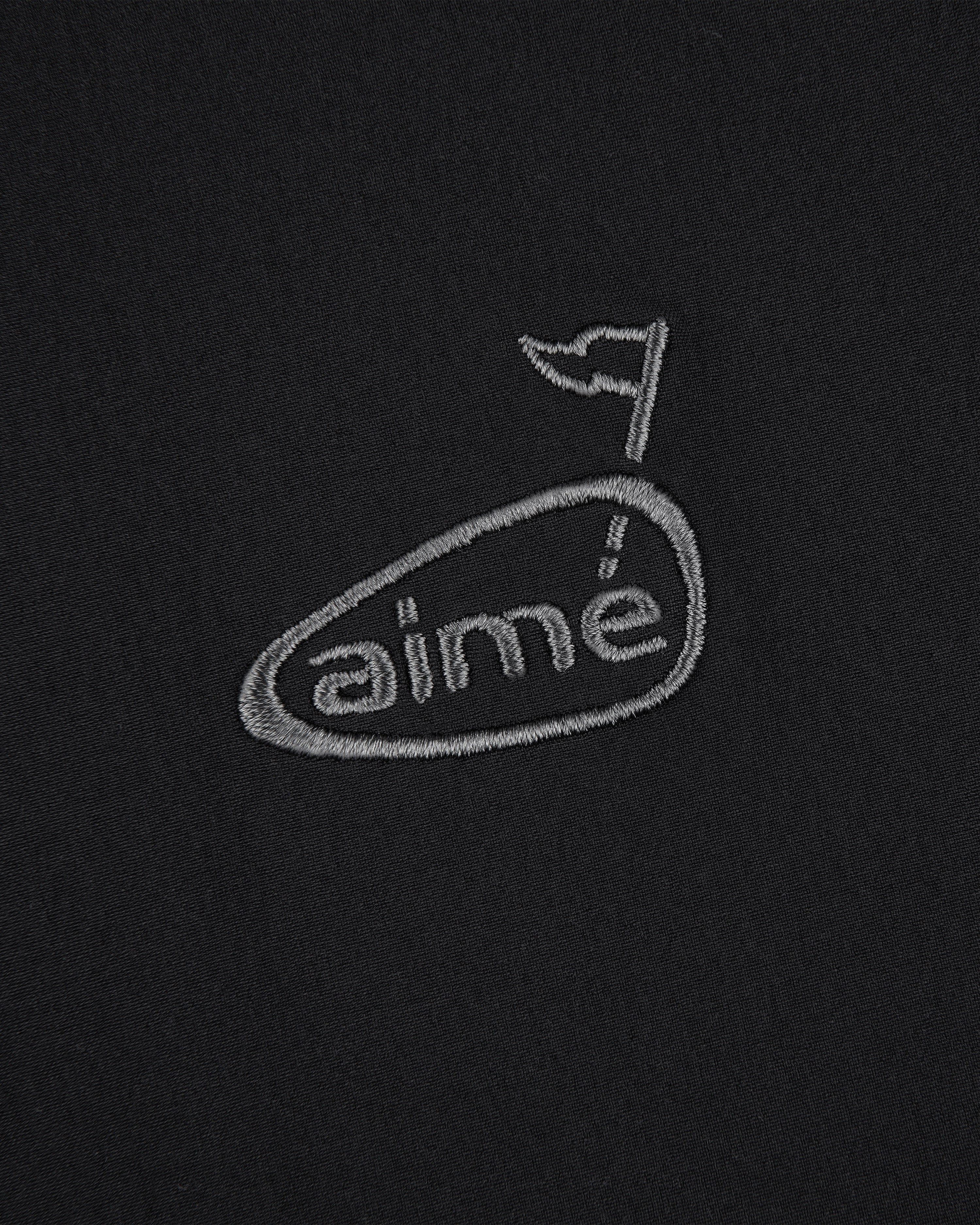 ALD Golf Cordura Tips Jacket: grey aimé logo with flag above the e, embroidered on plain black fabric.
