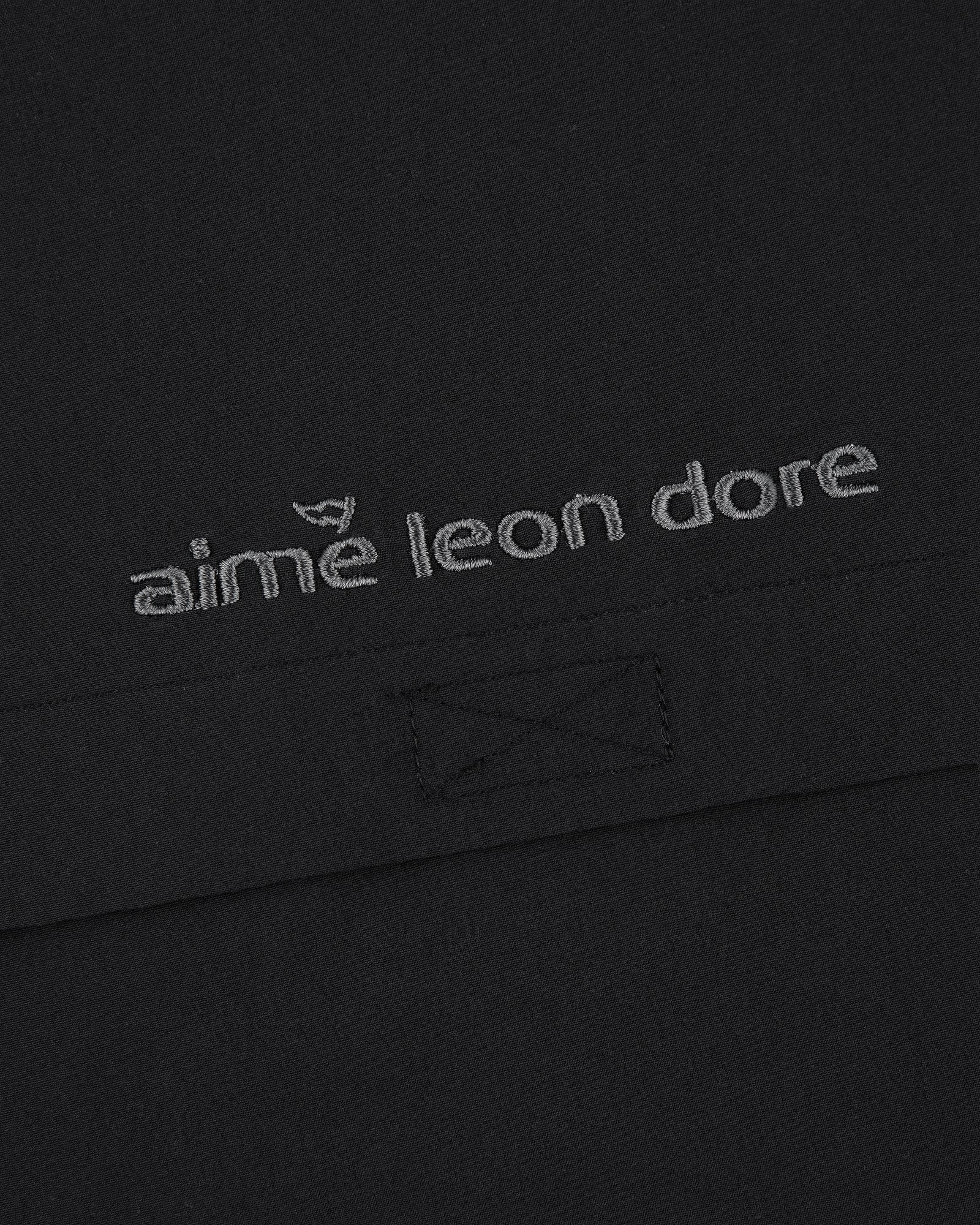 Close-up of black ALD Golf Cordura Tips Jacket with aimé leon dore embroidered in light gray thread.