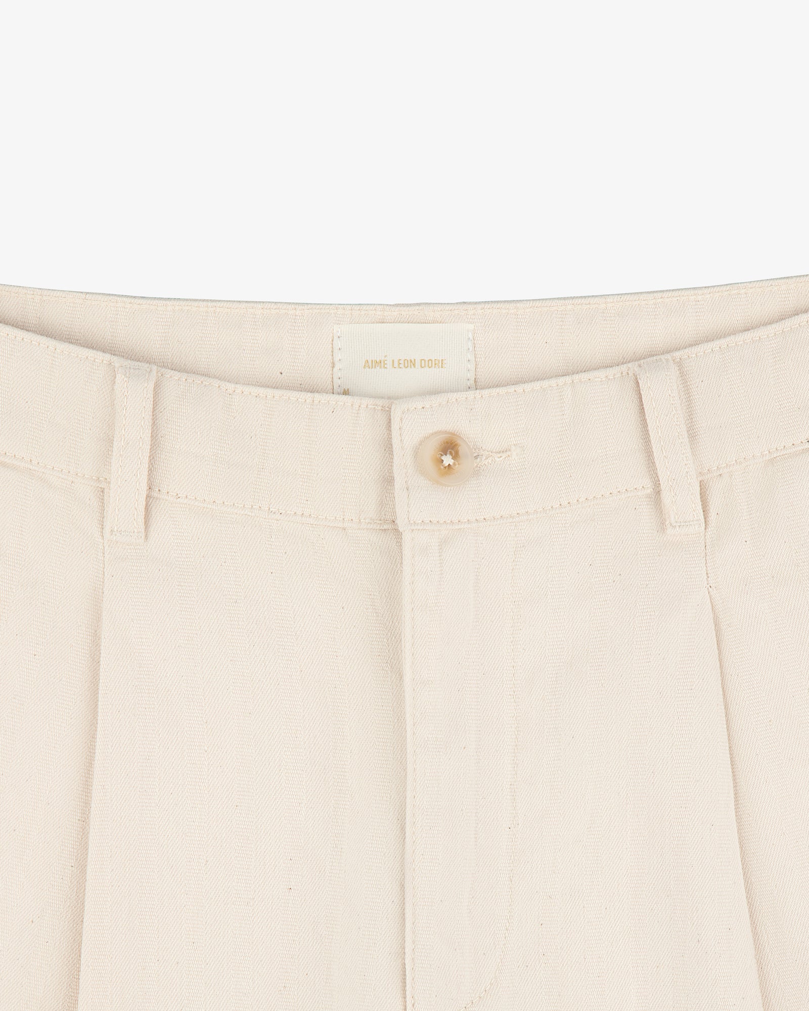 Close-up of Single Pleated Pant in cream with button closure, belt loops, and visible brand label on waistband.