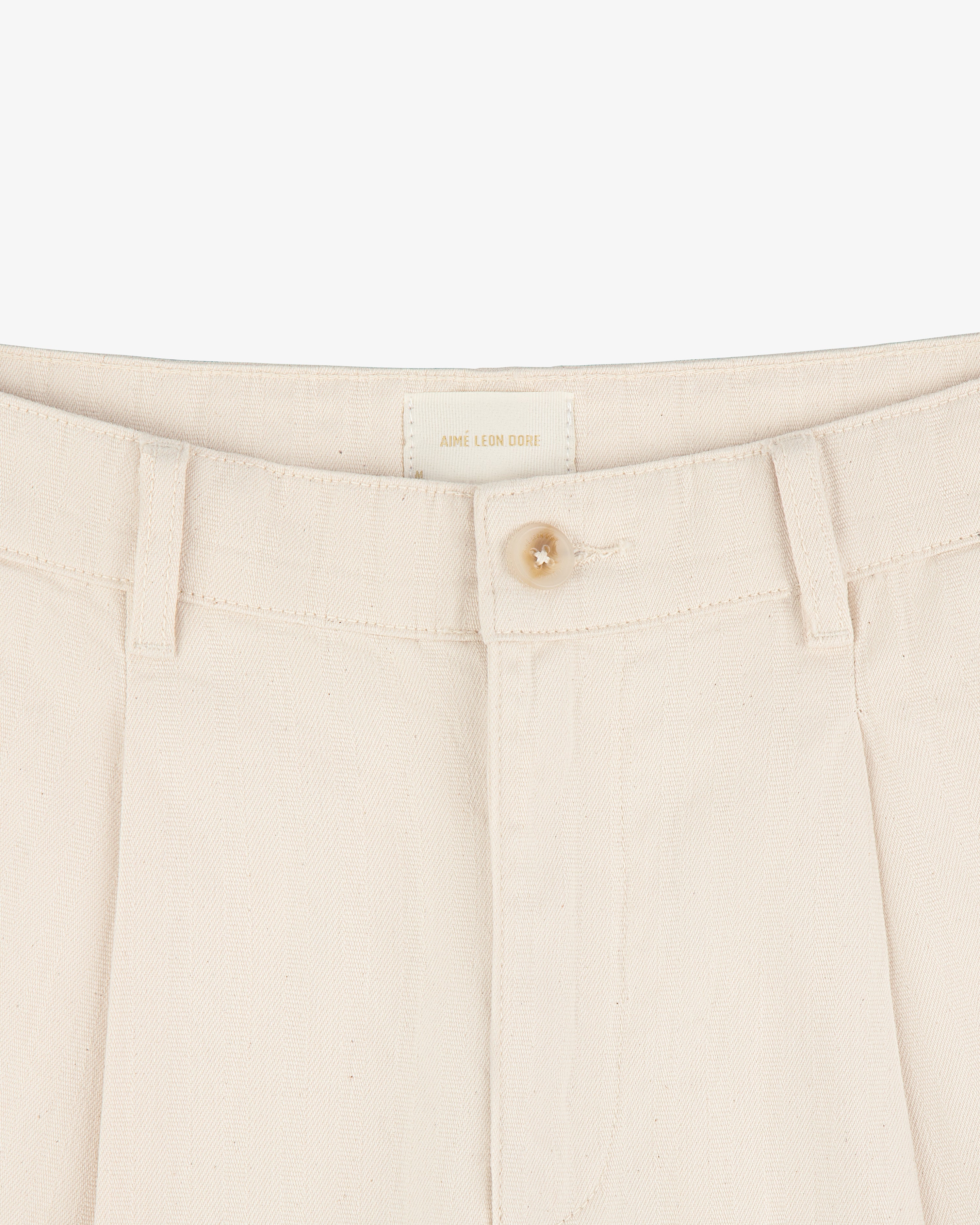 Close-up of Single Pleated Pant in cream with button closure, belt loops, and visible brand label on waistband.