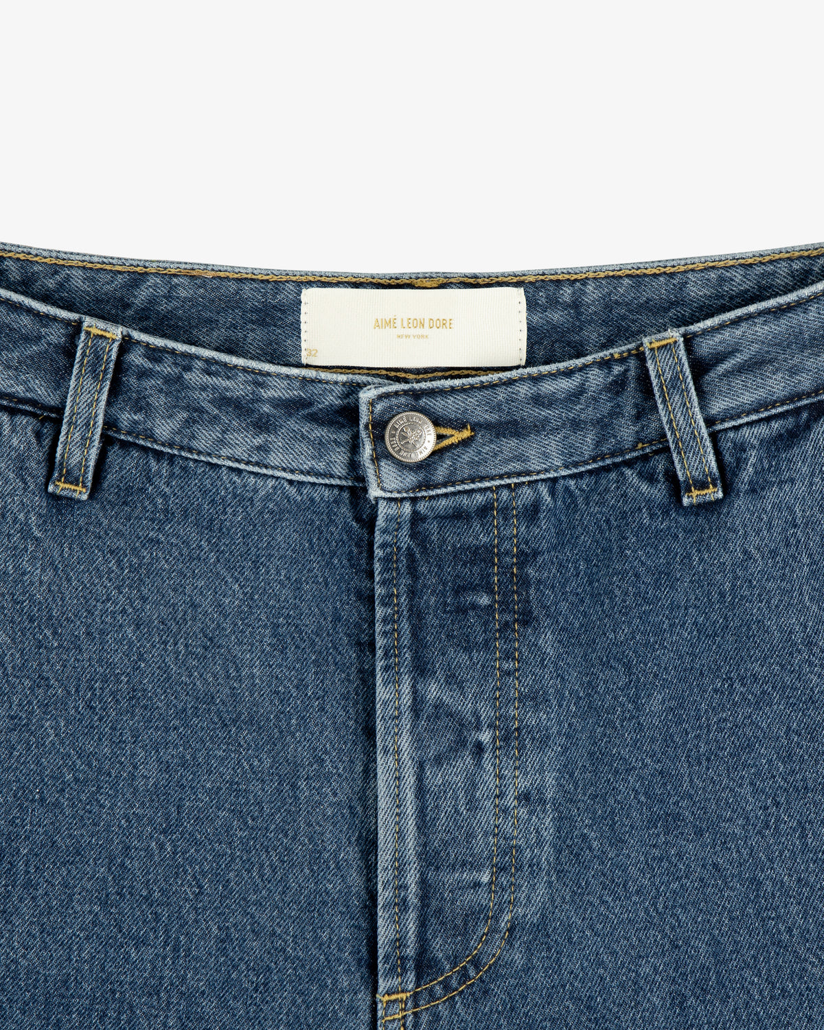 Close-up of Denim Carpenter Pant with button fly and white AIME LEON DORE label on the inner waistband.