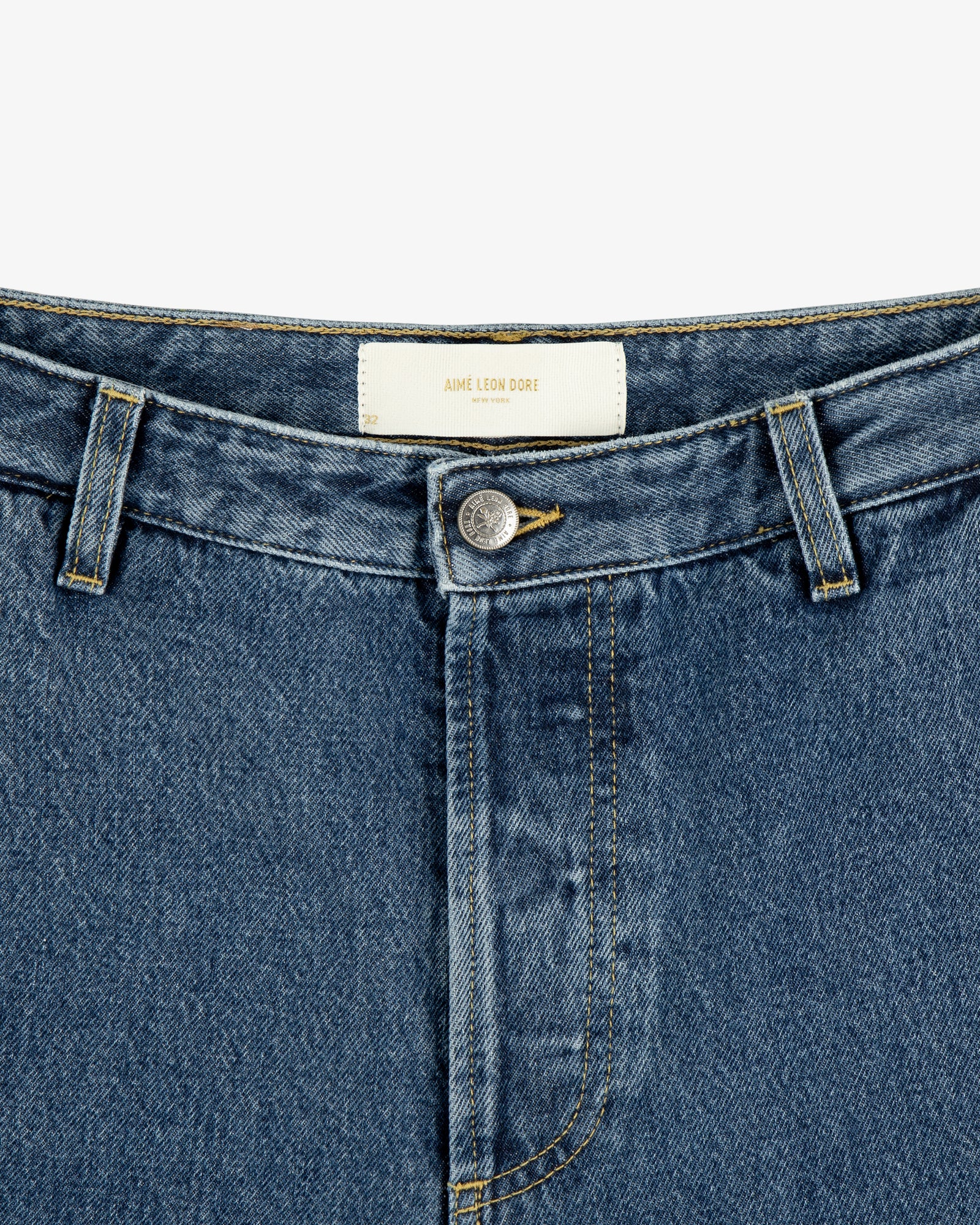 Close-up of Denim Carpenter Pant with button fly and white AIME LEON DORE label on the inner waistband.