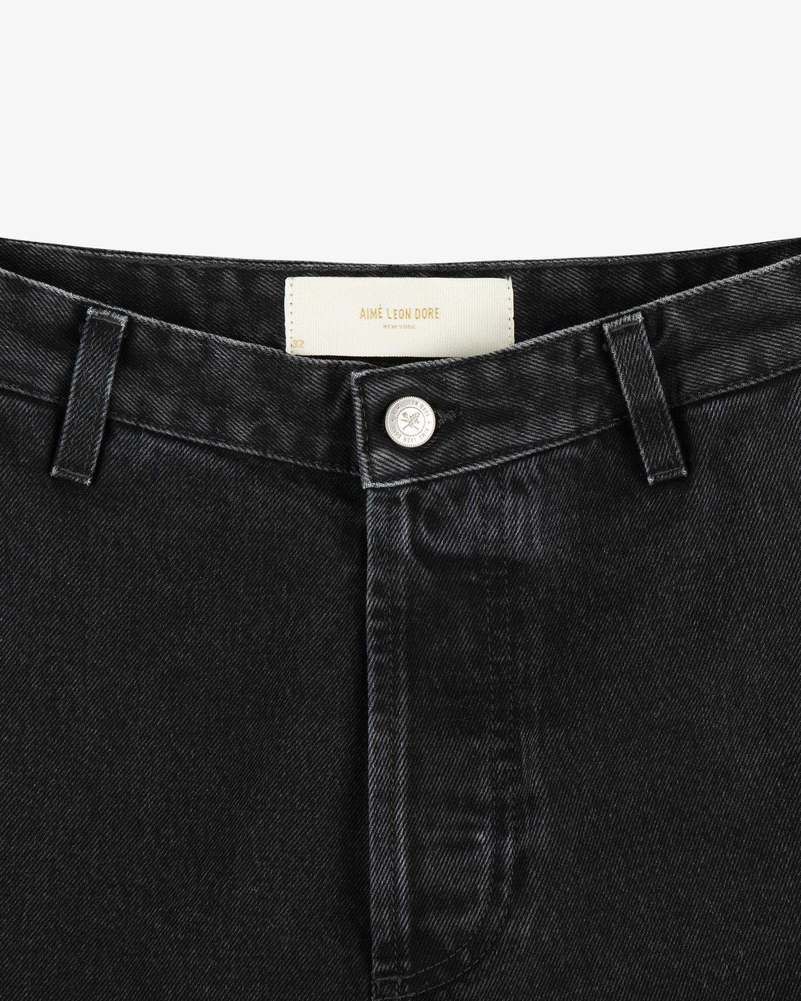 Close-up of the waistband and button of black Denim Carpenter Pant featuring an Aimé Leon Dore label inside.