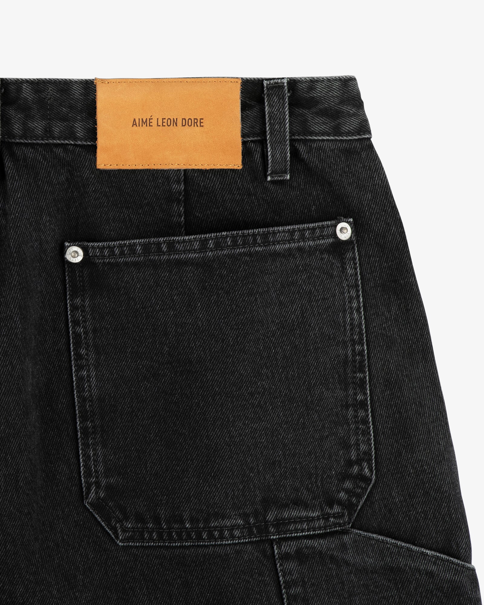 Close-up of Denim Carpenter Pant in black, showing a back pocket and tan leather AIME LEON DORE label.
