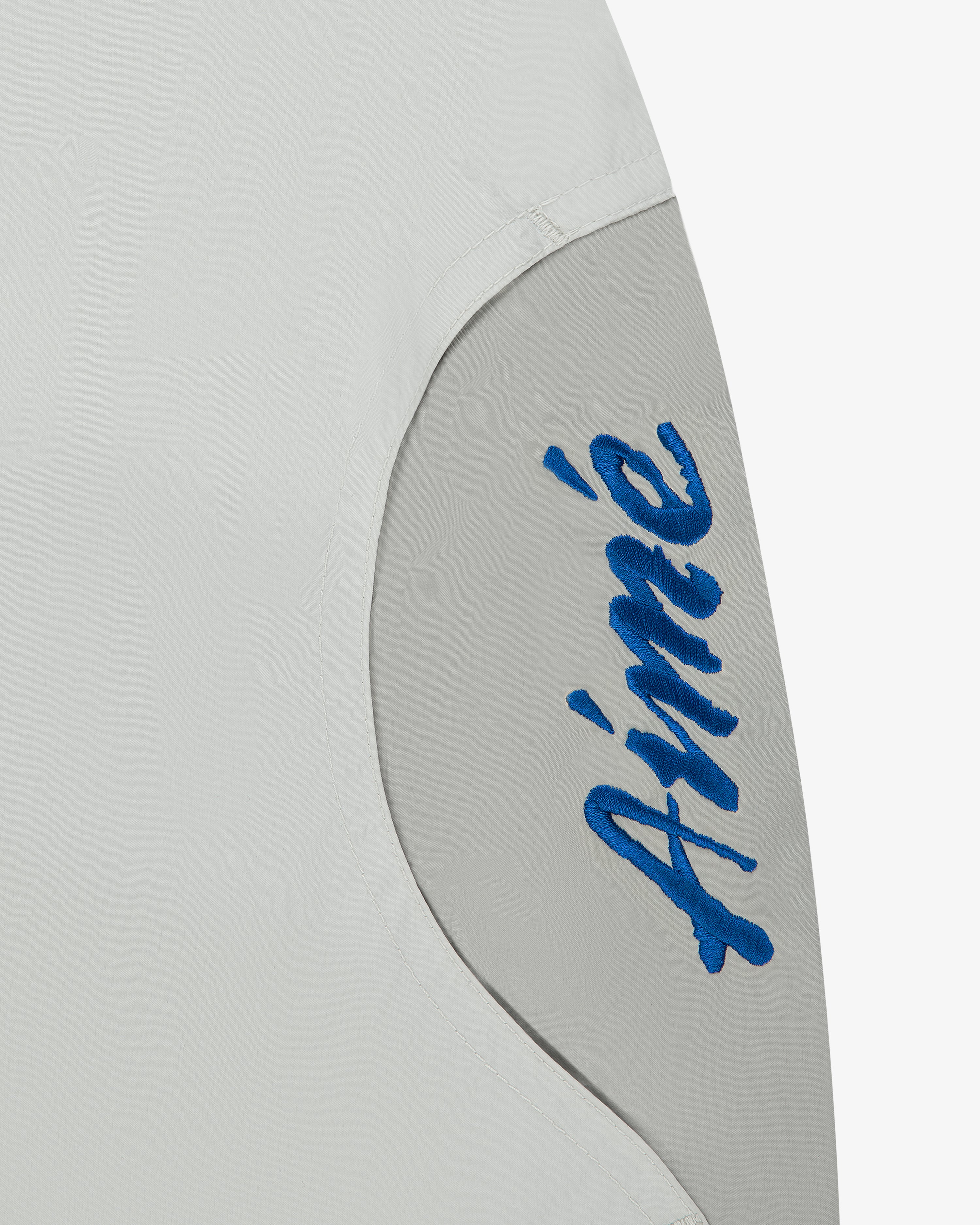 Close-up of a light gray Paneled Sport Short with Aimé stitched in blue cursive on a curved panel.