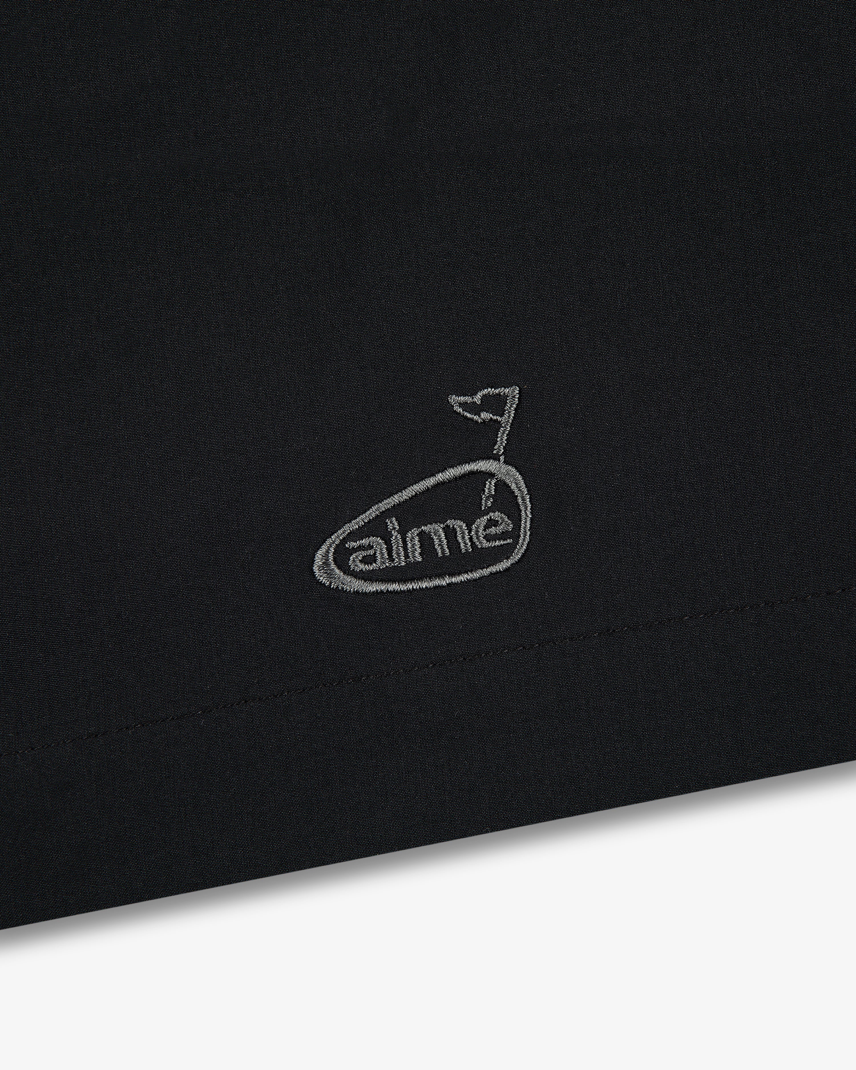 Black fabric with a small, white embroidered whale above “aimé” on the ALD Golf Performance Short.