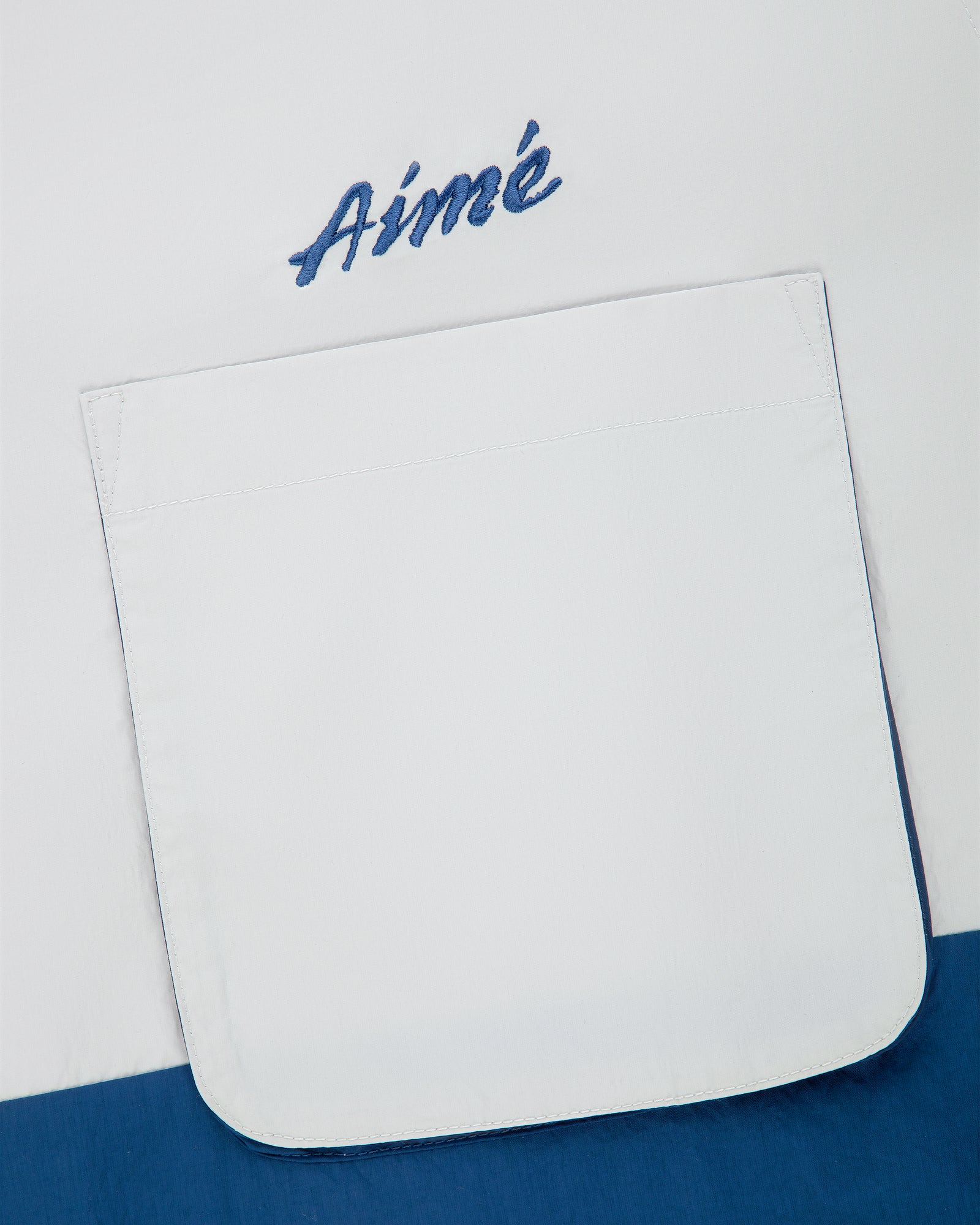 A Colorblock Sport Shirt with a white pocket and blue “Aimé” script embroidery above it.