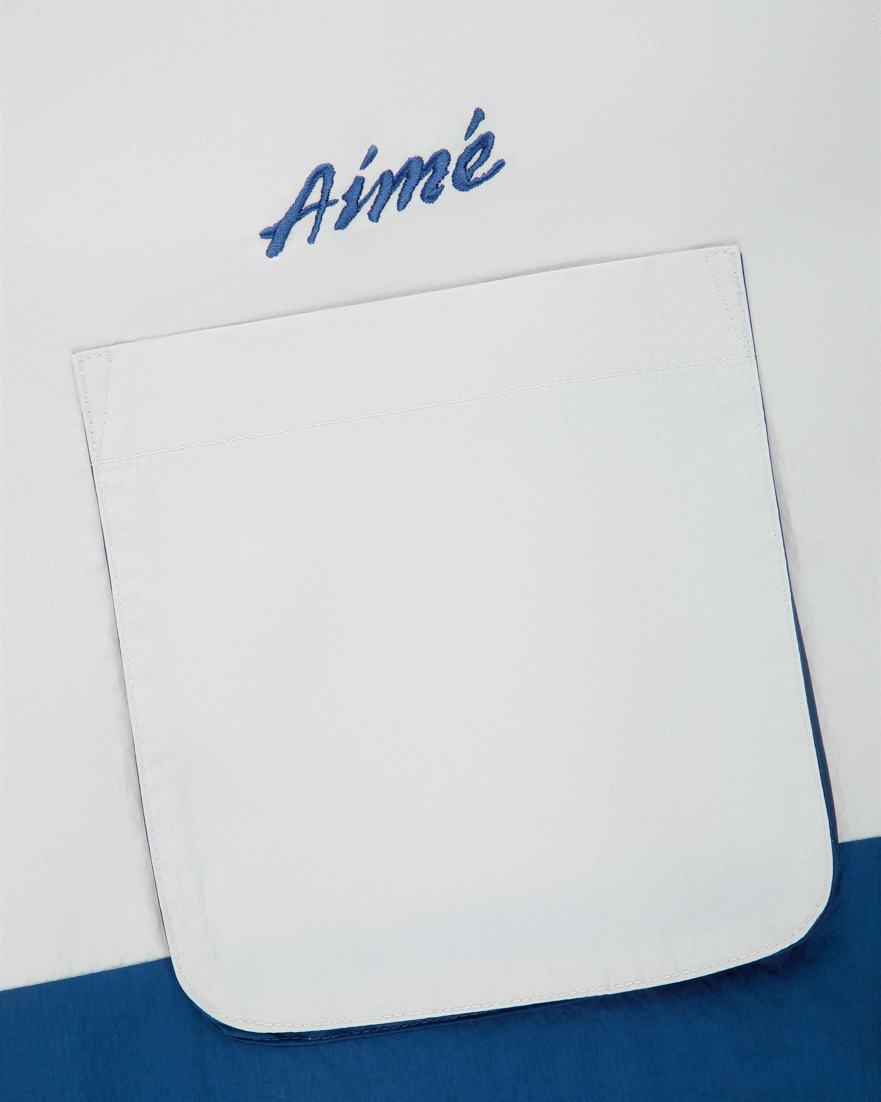 A Colorblock Sport Shirt with a white pocket and blue “Aimé” script embroidery above it.