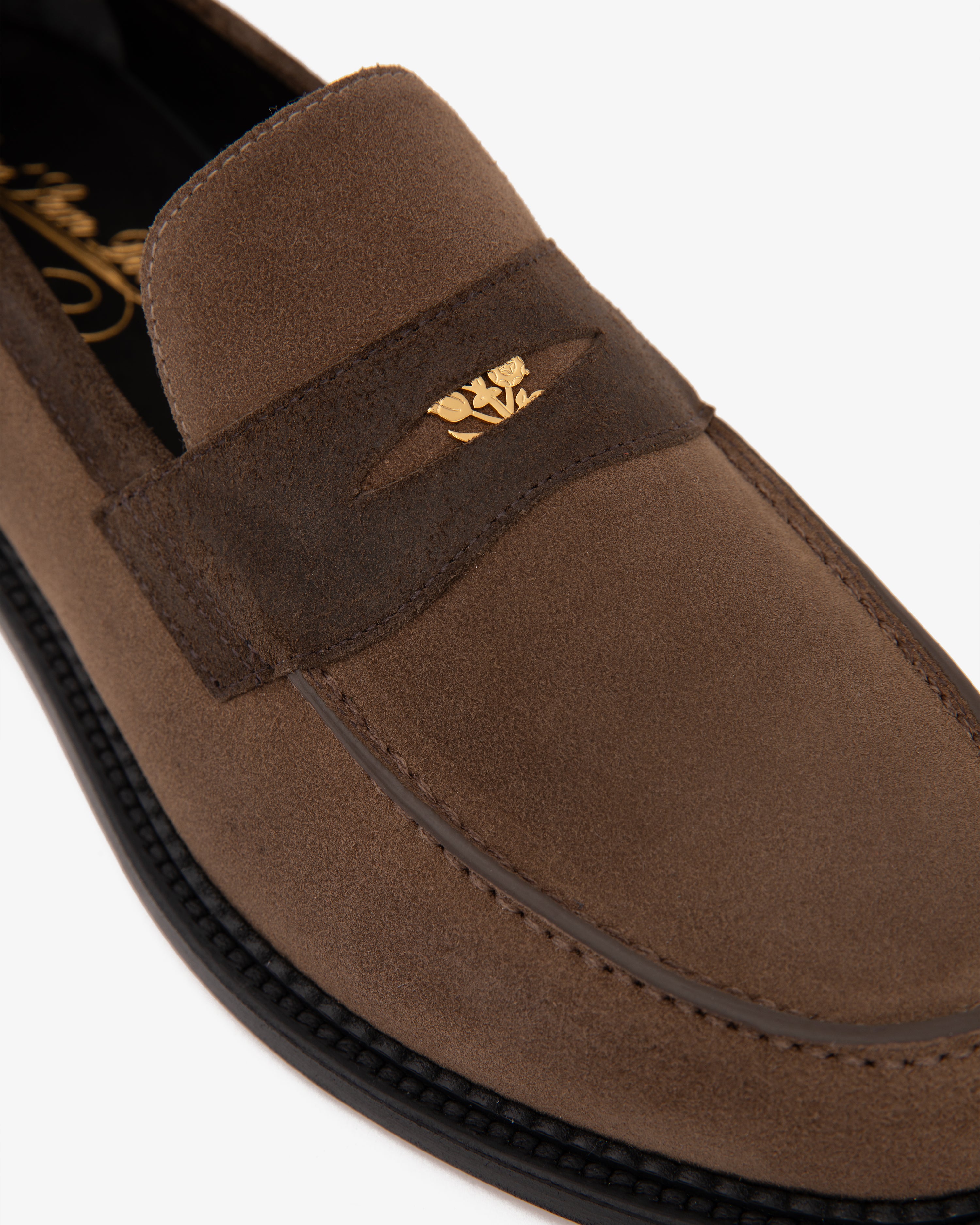 Suede Queens Crest Loafer in brown suede with gold emblem on strap, detailed with black stitching on the sole.