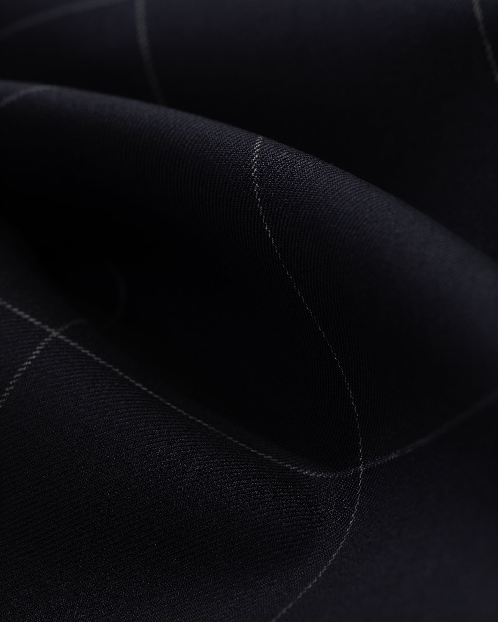 A close-up of the Windowpane Elasticated Waist Suit Trouser shows dark fabric with a subtle light grid and gentle folds.