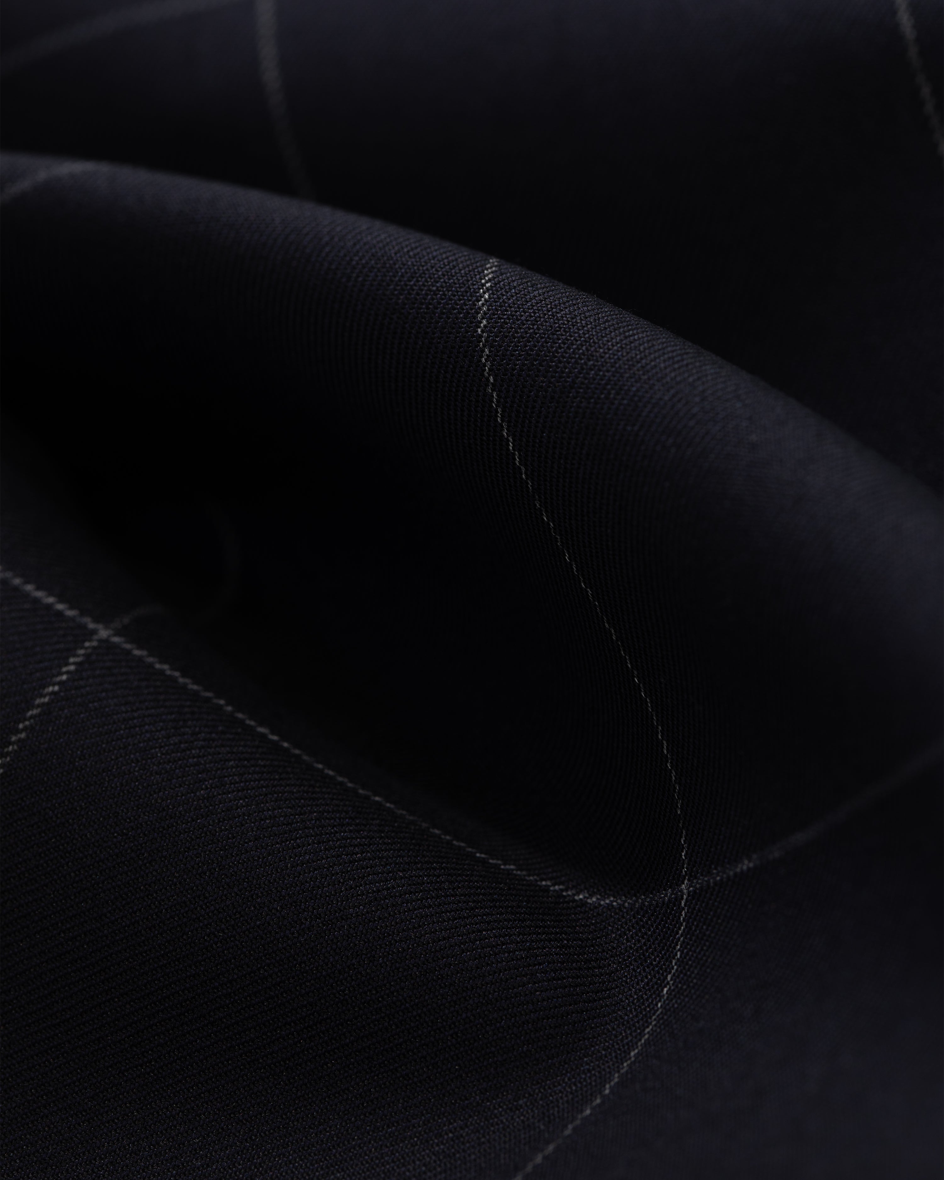 A close-up of the Windowpane Elasticated Waist Suit Trouser shows dark fabric with a subtle light grid and gentle folds.