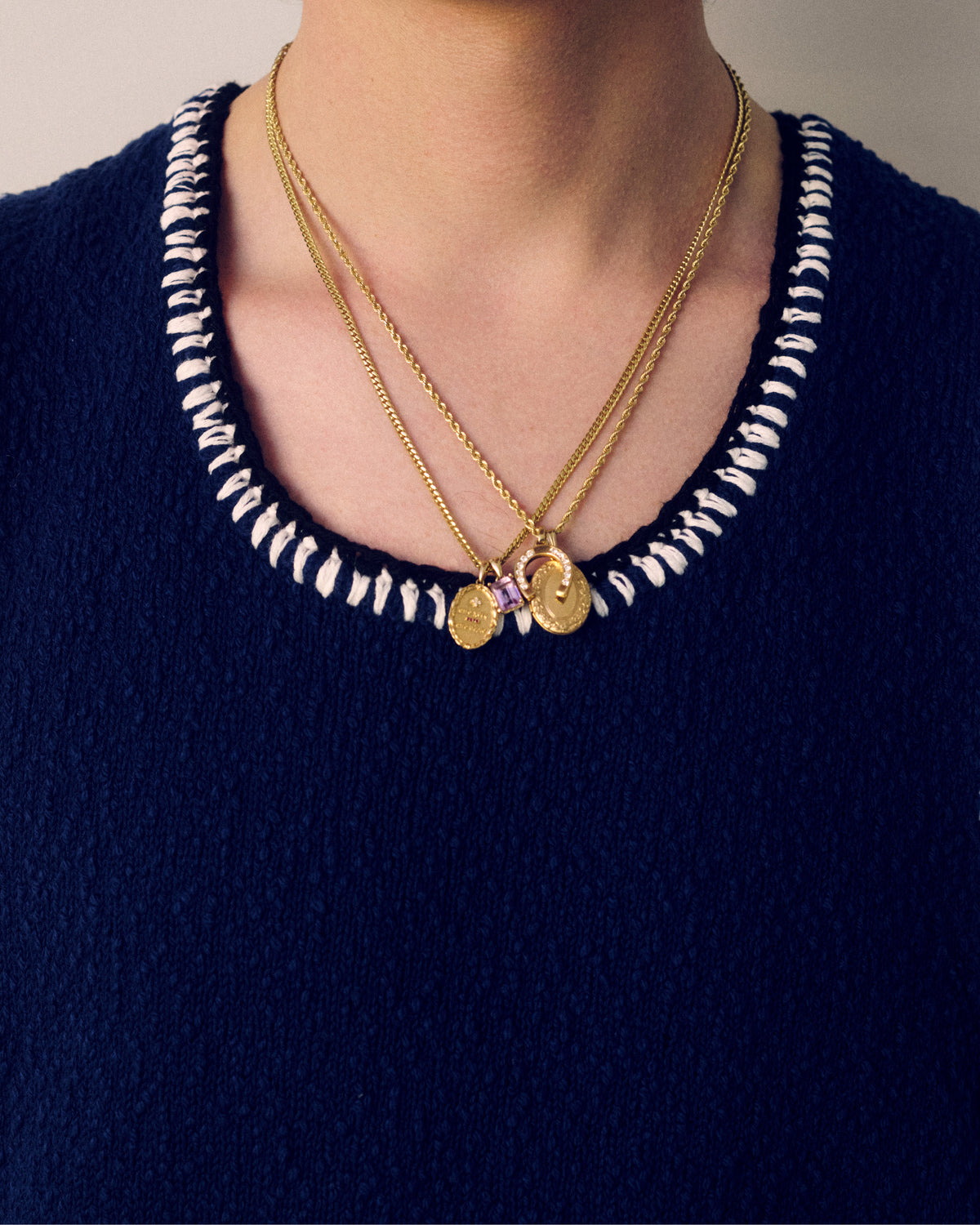Person wearing a navy blue textured top with a woven white neckline and a 14Kt Gold Gemstone Pendant.