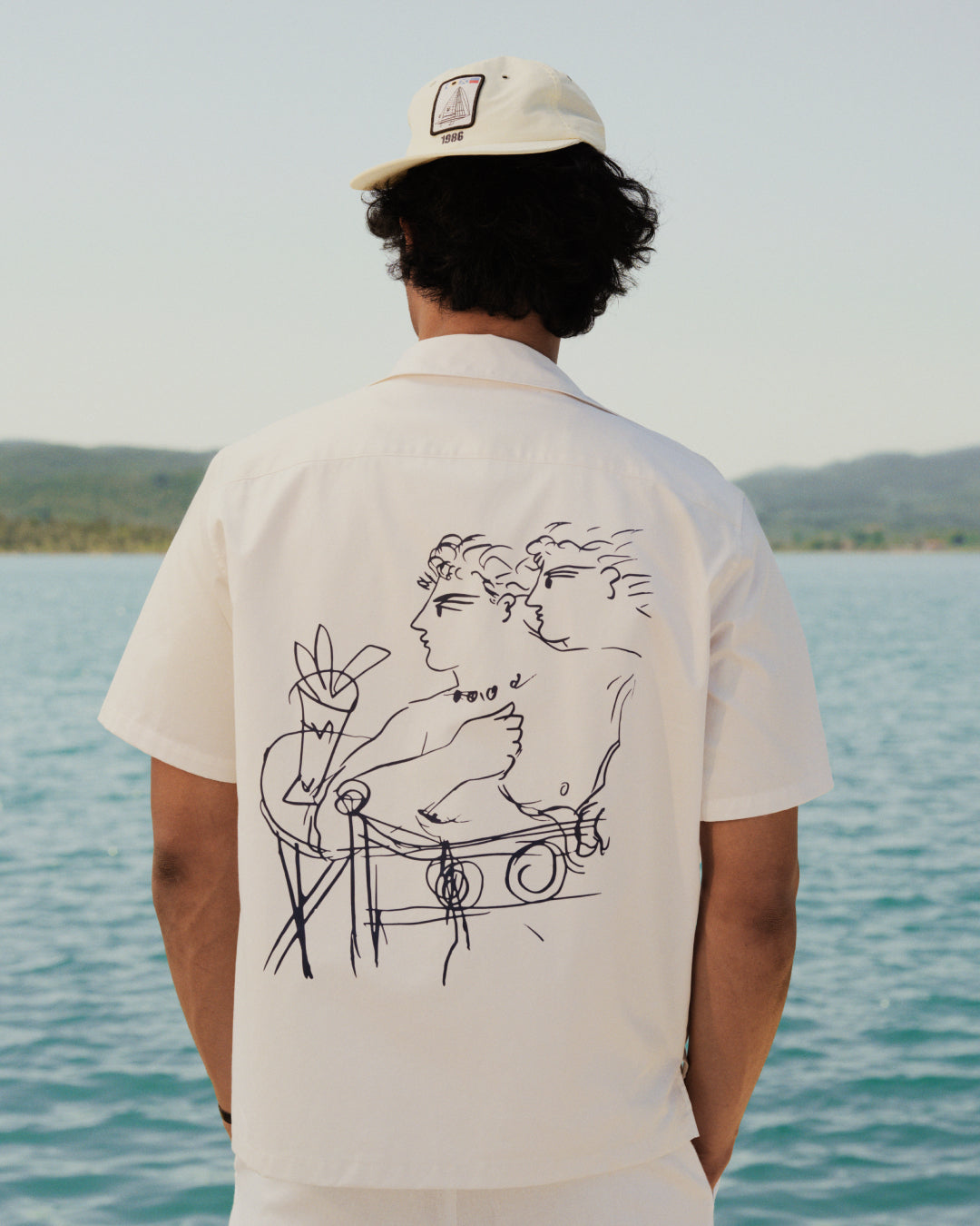 Person in a Nylon Deck Hat stands by blue water, facing away from the camera.