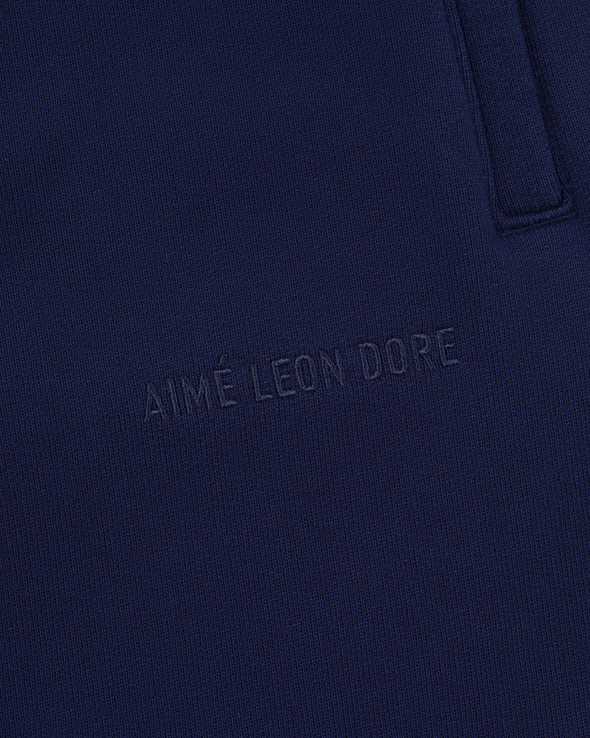 Close-up of Tonal Logo Sweatpants in navy blue with AIMÉ LEON DORE subtly embossed on the fabric.
