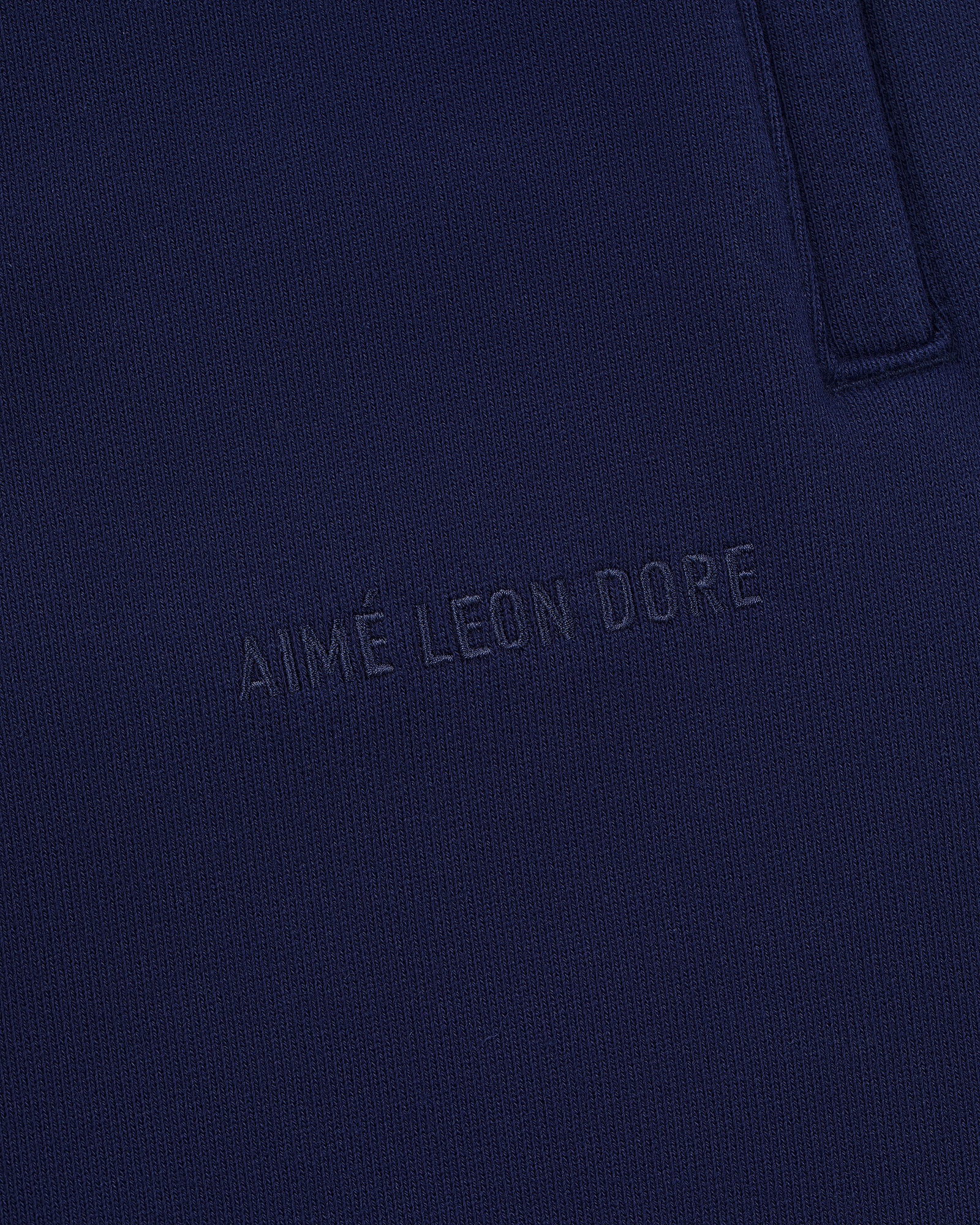 Close-up of Tonal Logo Sweatpants in navy blue with AIMÉ LEON DORE subtly embossed on the fabric.