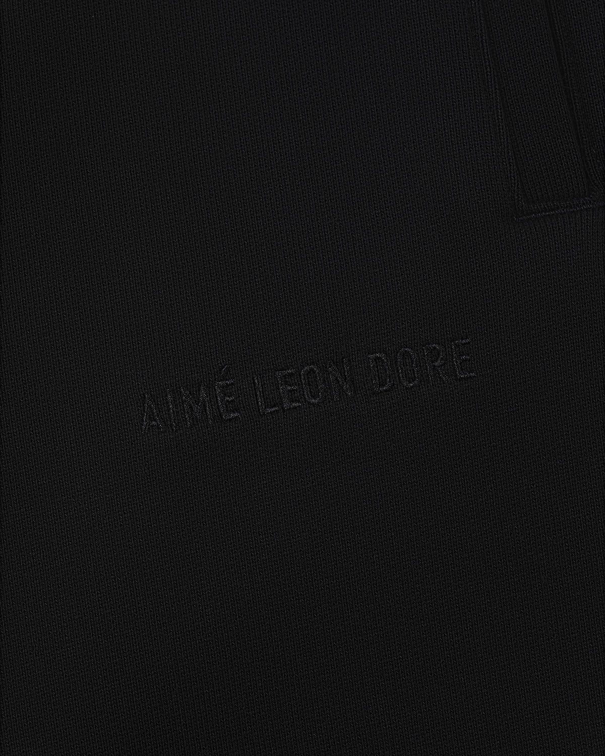Close-up of Tonal Logo Sweatpants with AIMÉ LEON DORE subtly embroidered on black textured fabric.
