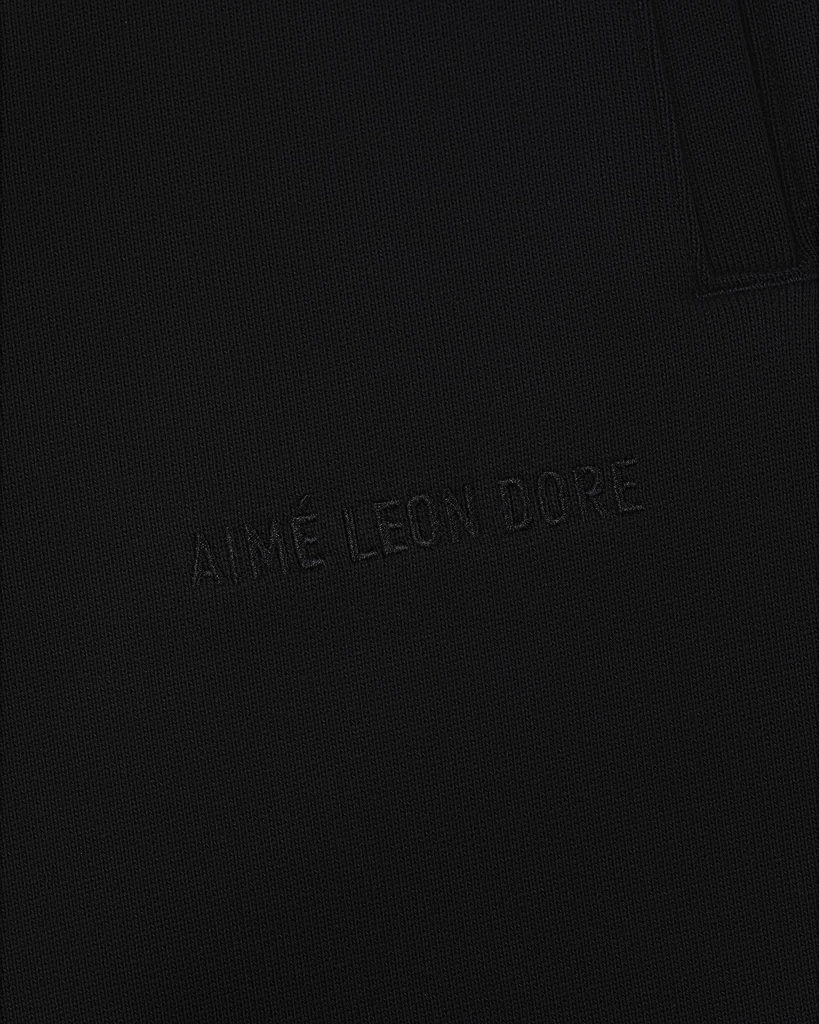 Close-up of Tonal Logo Sweatpants with AIMÉ LEON DORE subtly embroidered on black textured fabric.