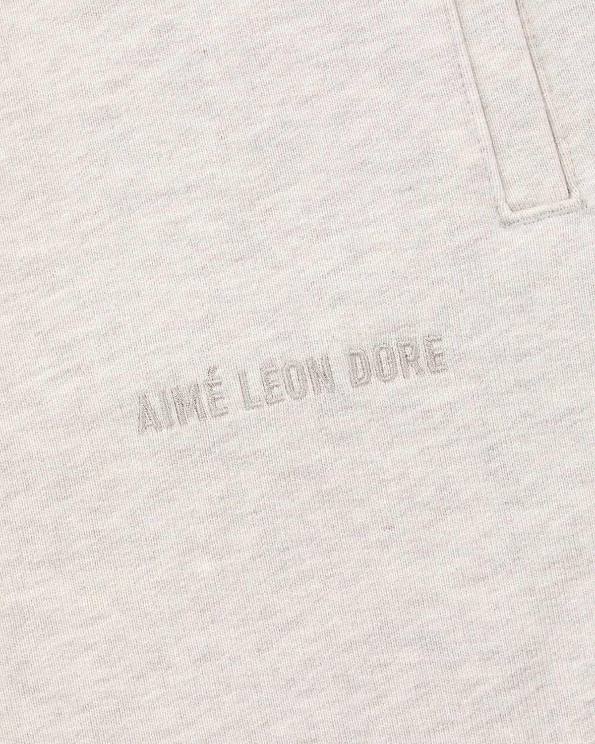 Close-up of oatmeal Tonal Logo Sweatpants with AIMÉ LEON DORE text embroidered near a vertical pocket seam.