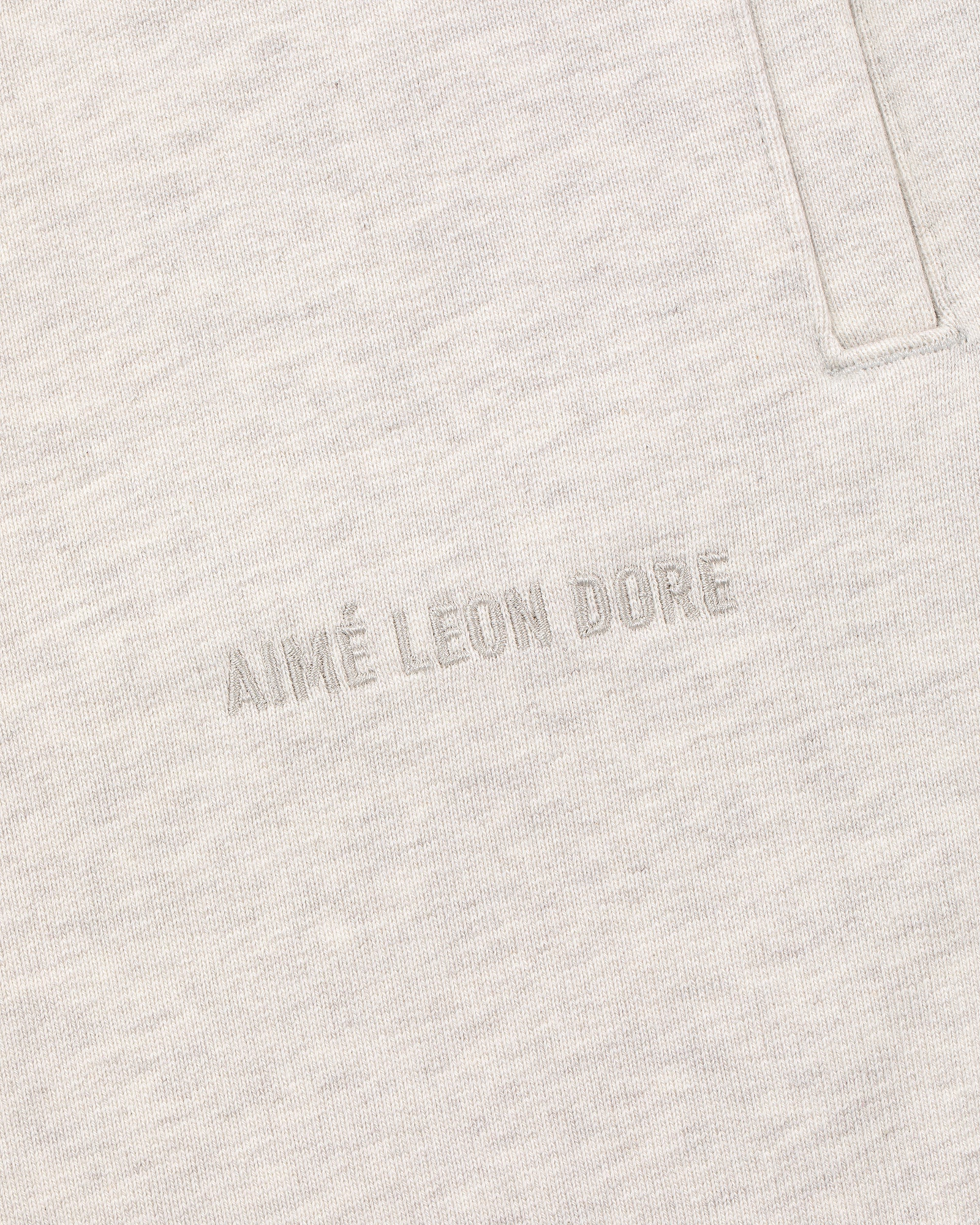 Close-up of oatmeal Tonal Logo Sweatpants with AIMÉ LEON DORE text embroidered near a vertical pocket seam.
