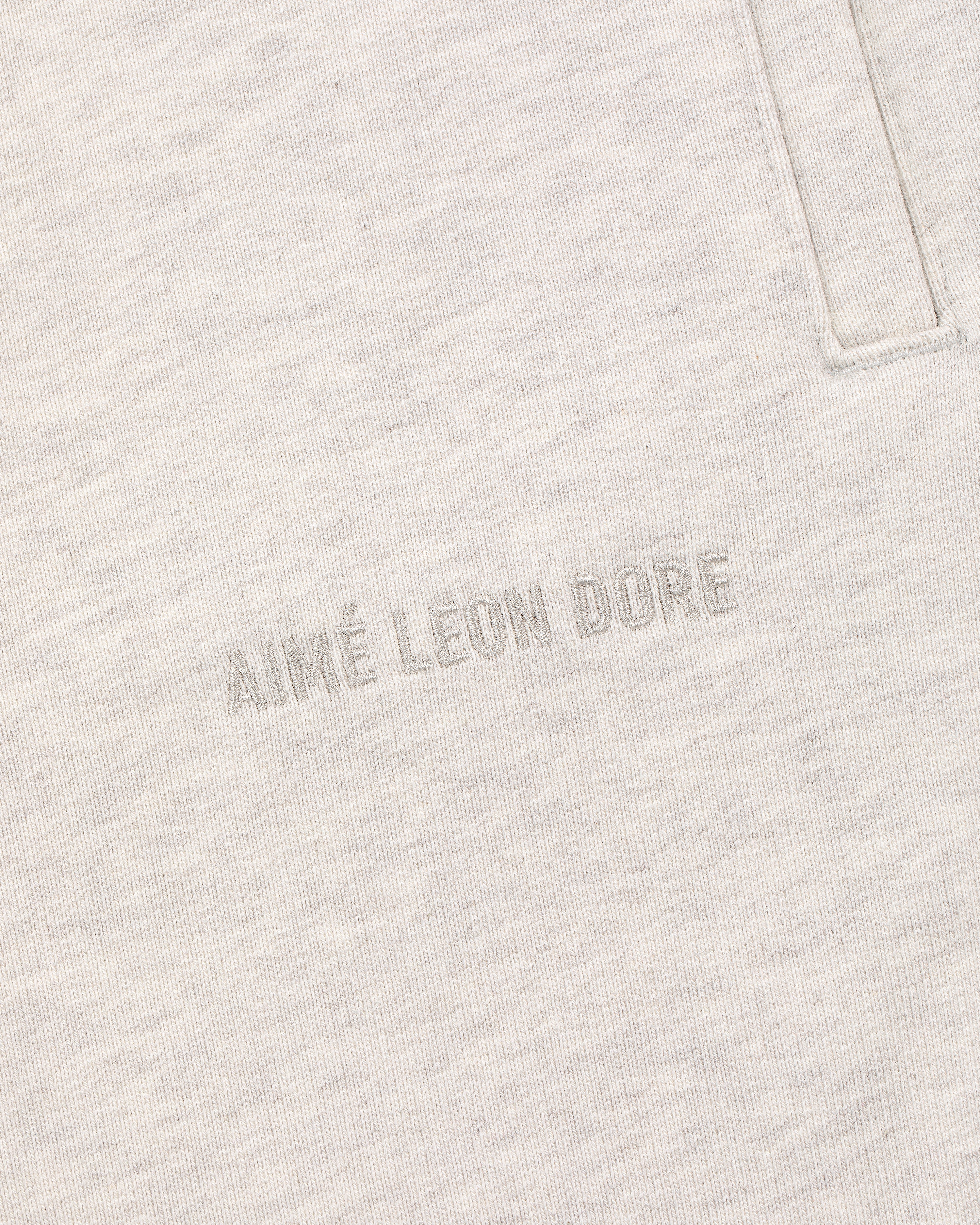 Close-up of oatmeal Tonal Logo Sweatpants with AIMÉ LEON DORE text embroidered near a vertical pocket seam.