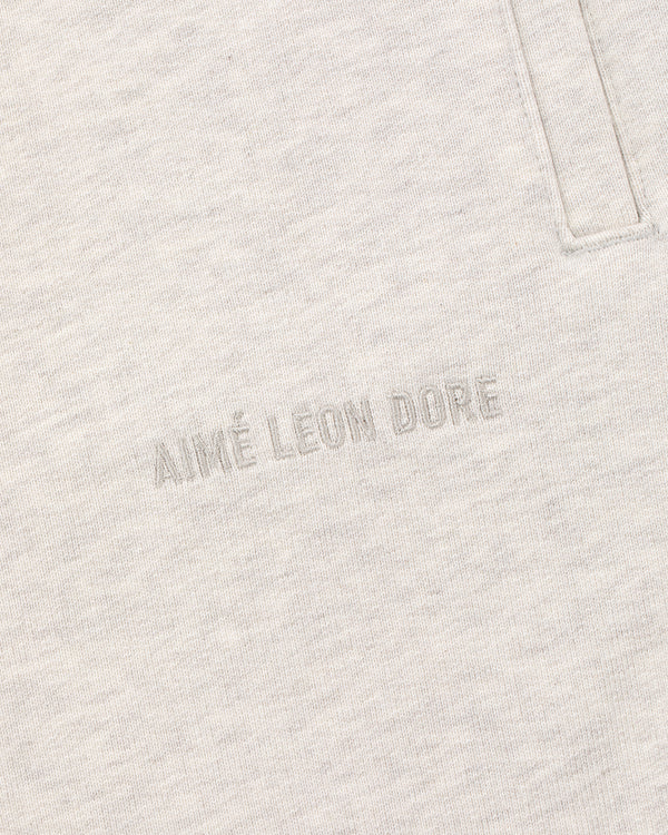 Close-up of oatmeal Tonal Logo Sweatpants with AIMÉ LEON DORE text embroidered near a vertical pocket seam.
