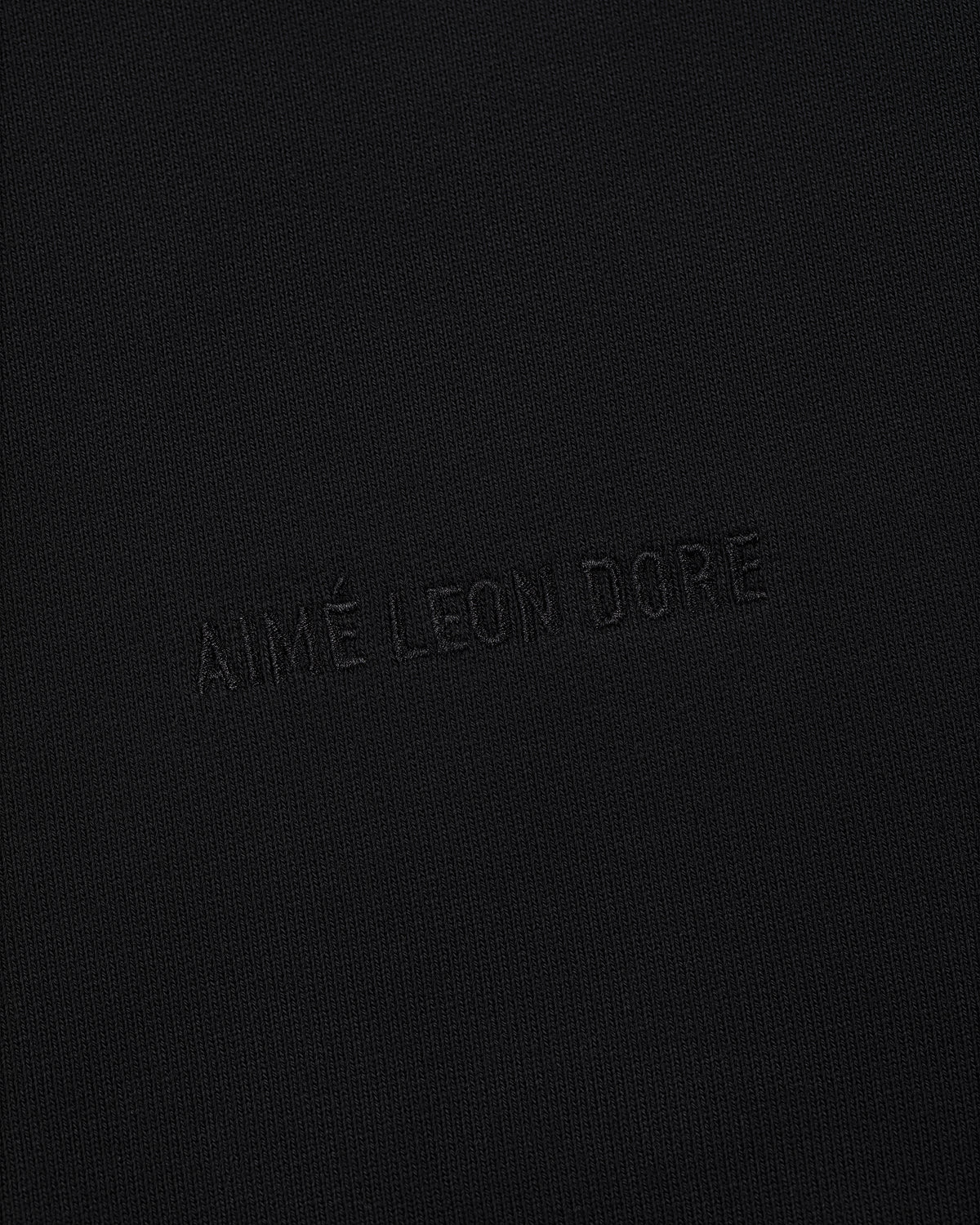 The Tonal Logo Hoodie features black fabric with a subtle, matching black AIMÉ LEON DORE embossed logo for a minimal look.