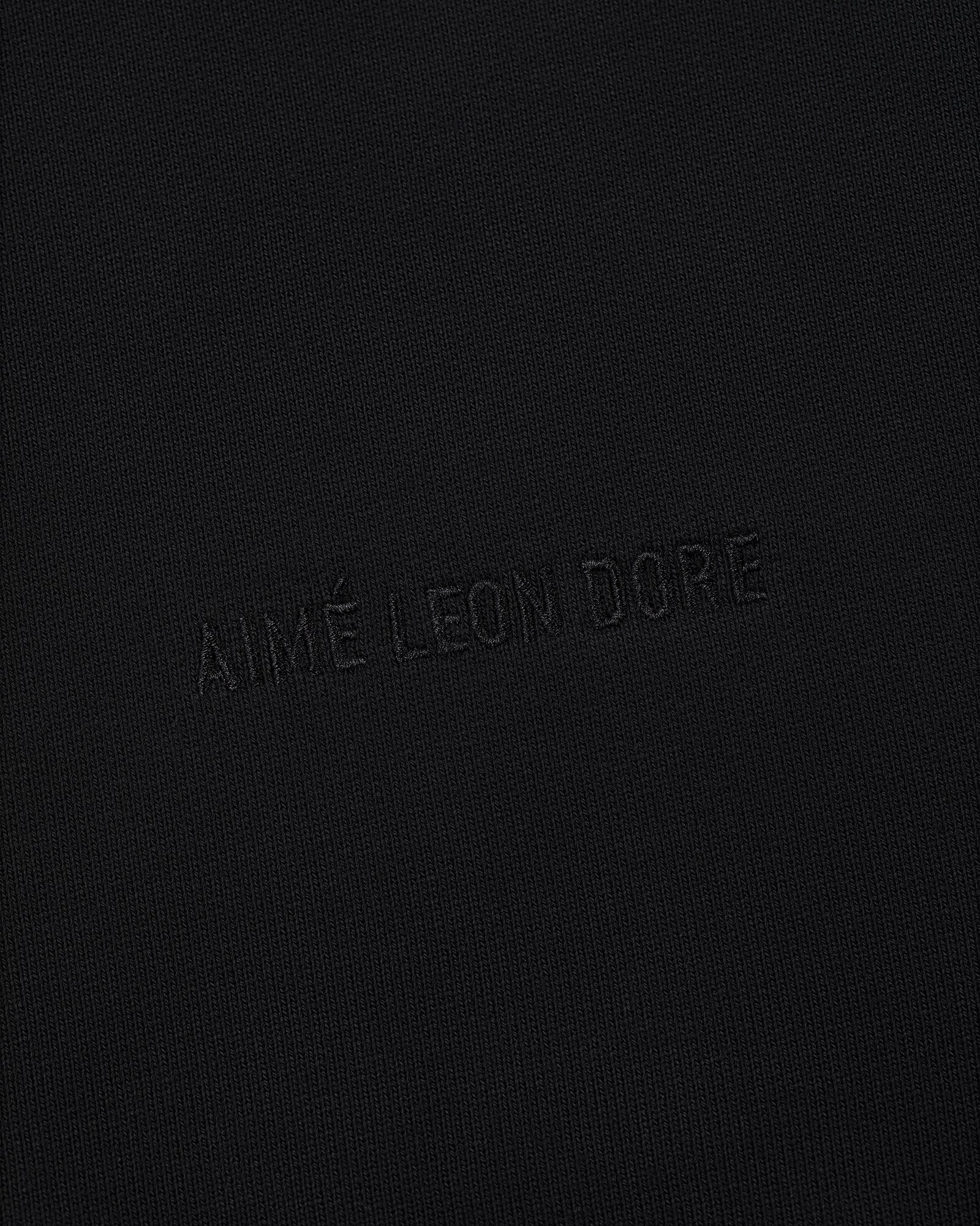 The Tonal Logo Hoodie features black fabric with a subtle, matching black AIMÉ LEON DORE embossed logo for a minimal look.