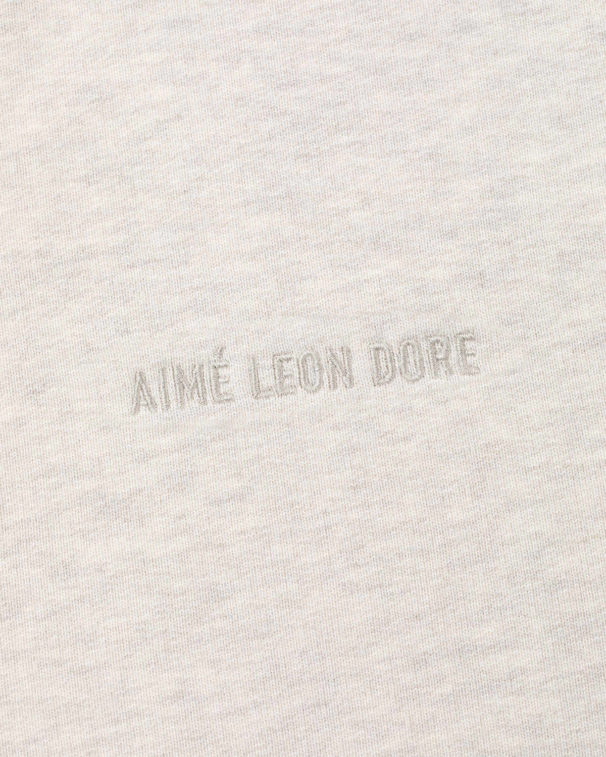 Close-up of the Tonal Logo Hoodie’s light gray fabric with matching AIMÉ LEON DORE embroidery at the center.