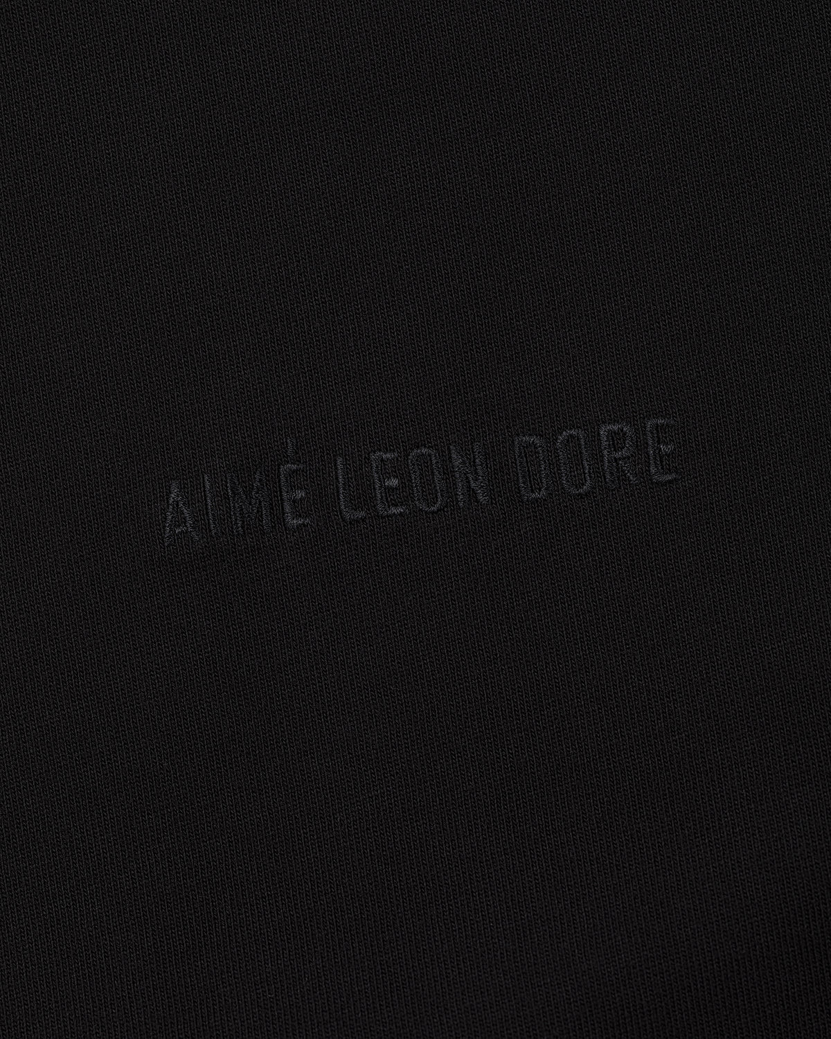 Close-up of black fabric on the Long-Sleeve Tonal Logo Tee with AIMÉ LEON DORE subtly embossed at the center.