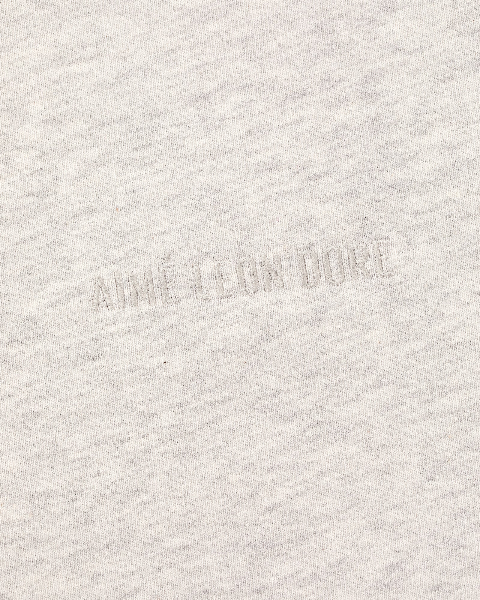 Close-up of the Long-Sleeve Tonal Logo Tee's light gray fabric with an embossed AIMÉ LEON DORE logo blending in.