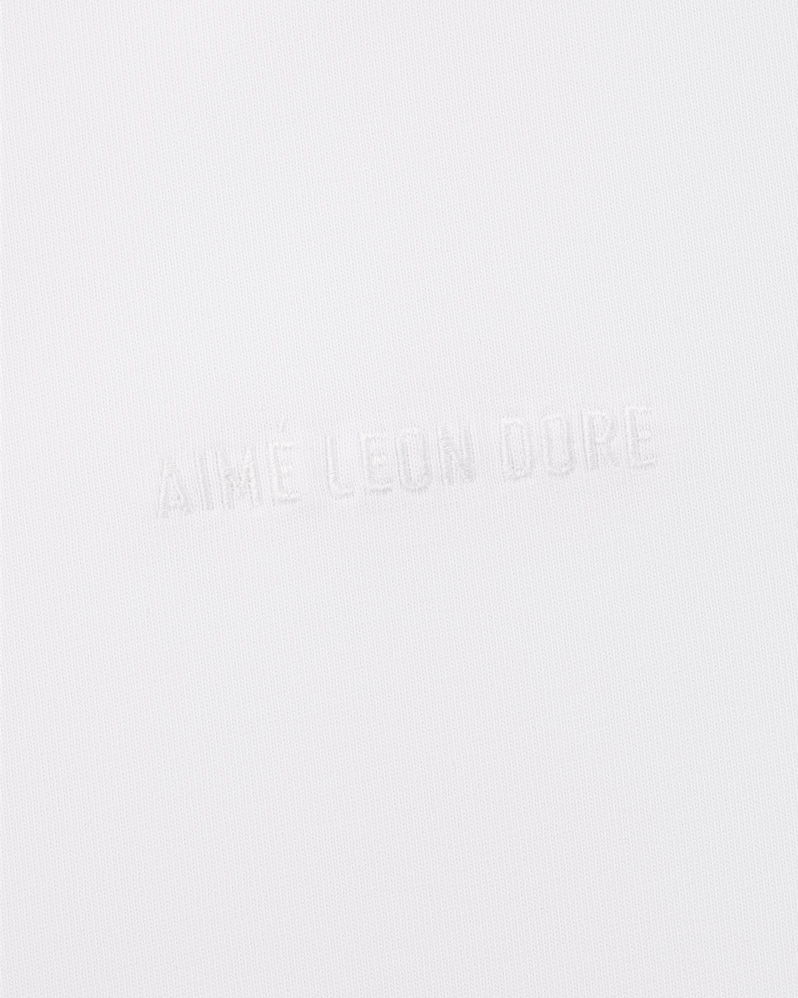 The Tonal Logo Tee features white fabric with subtle, embossed AIMÉ LEON DORE text in all caps across the center.