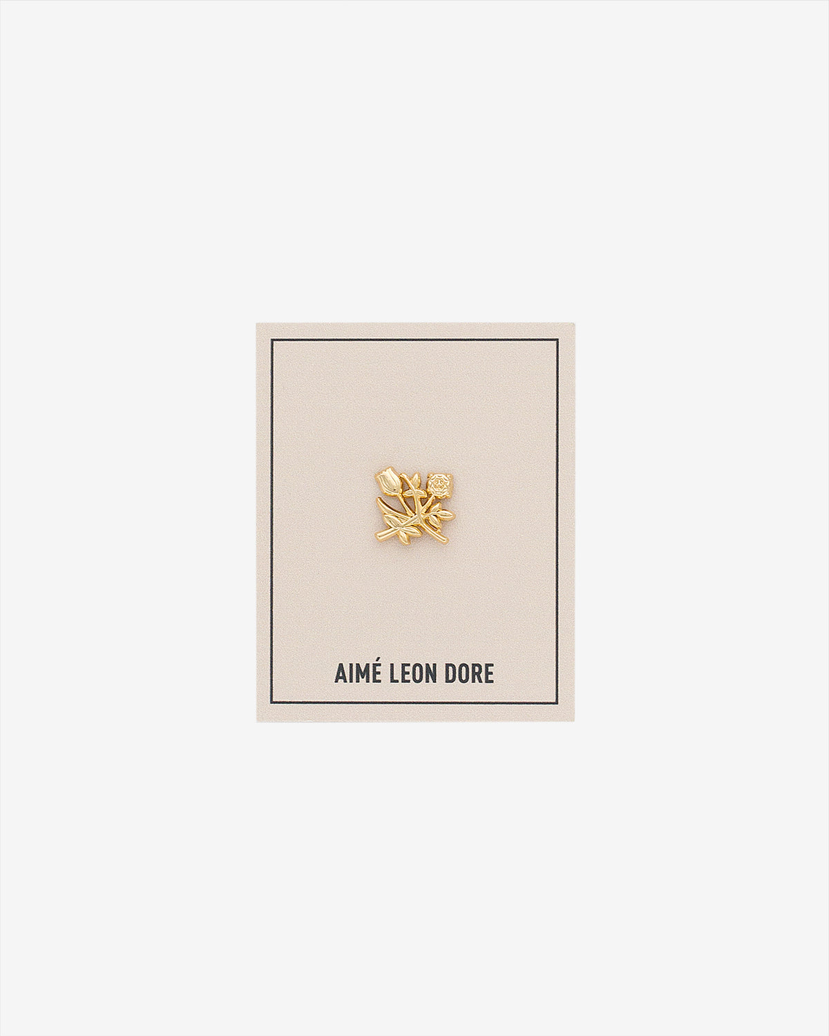 An ALD Pin shaped like a gold leaf is displayed on a beige AIMÉ LEON DORE card against a white background.