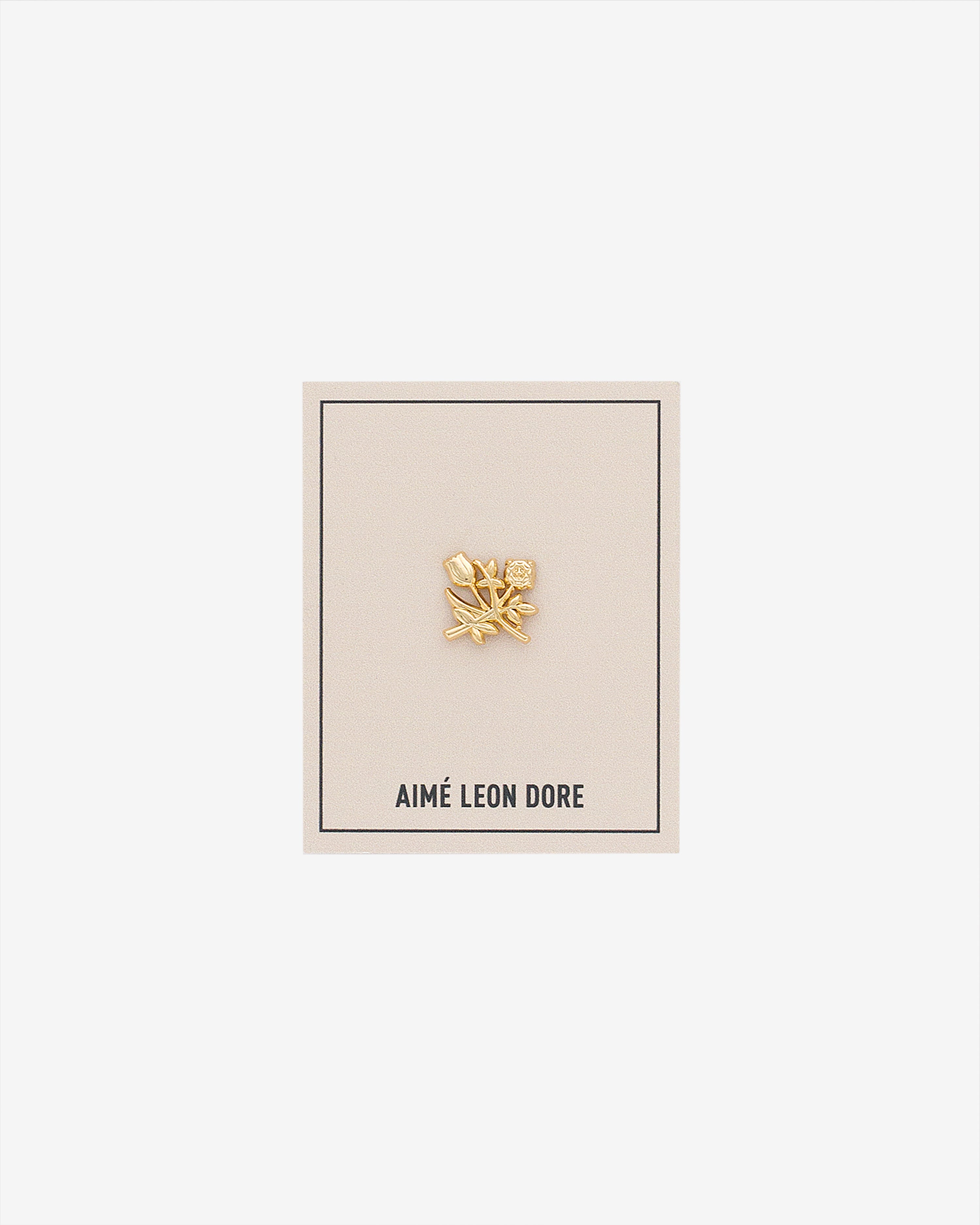 An ALD Pin shaped like a gold leaf is displayed on a beige AIMÉ LEON DORE card against a white background.
